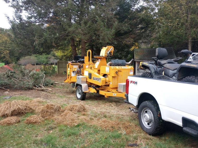 White pickup truck towing a Bandit wood chipper at a residential job site