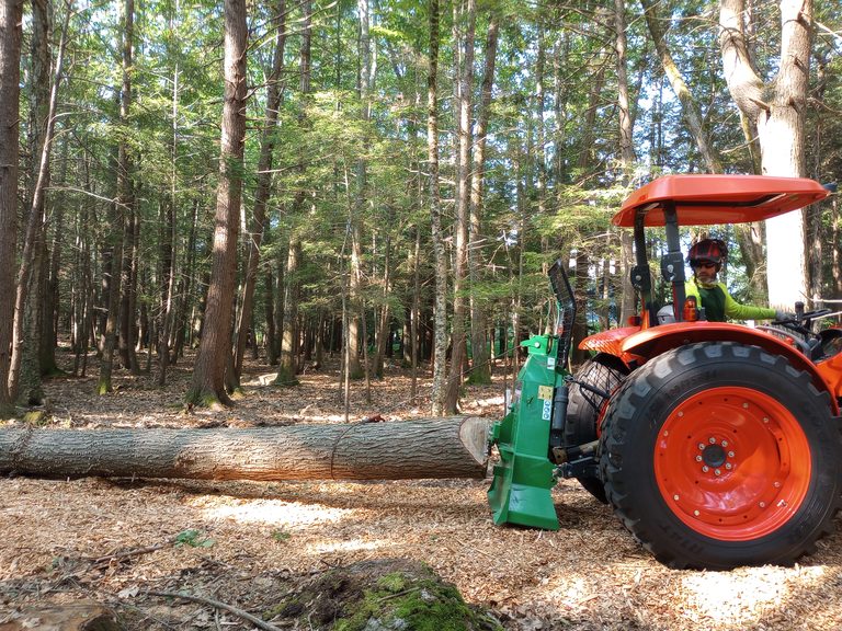 NFS owner operating a compact tractor to drag a log through the woods