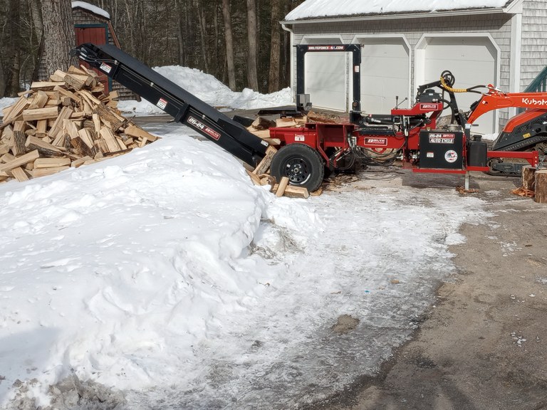 Firewood being processed with a log splitter on a snowy winter job site