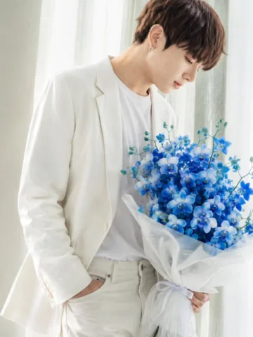 A close-up fashion editorial shot of BTS Jeon Jungkook holding a large bouquet o