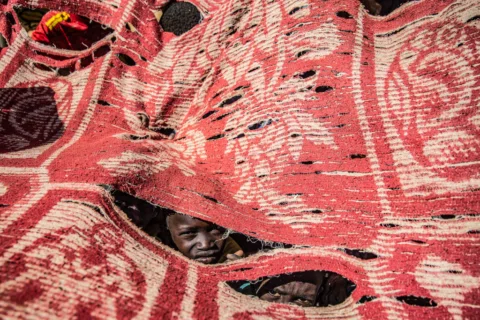 Two children take shelter beneath pieces of fabric strung together to form a mak