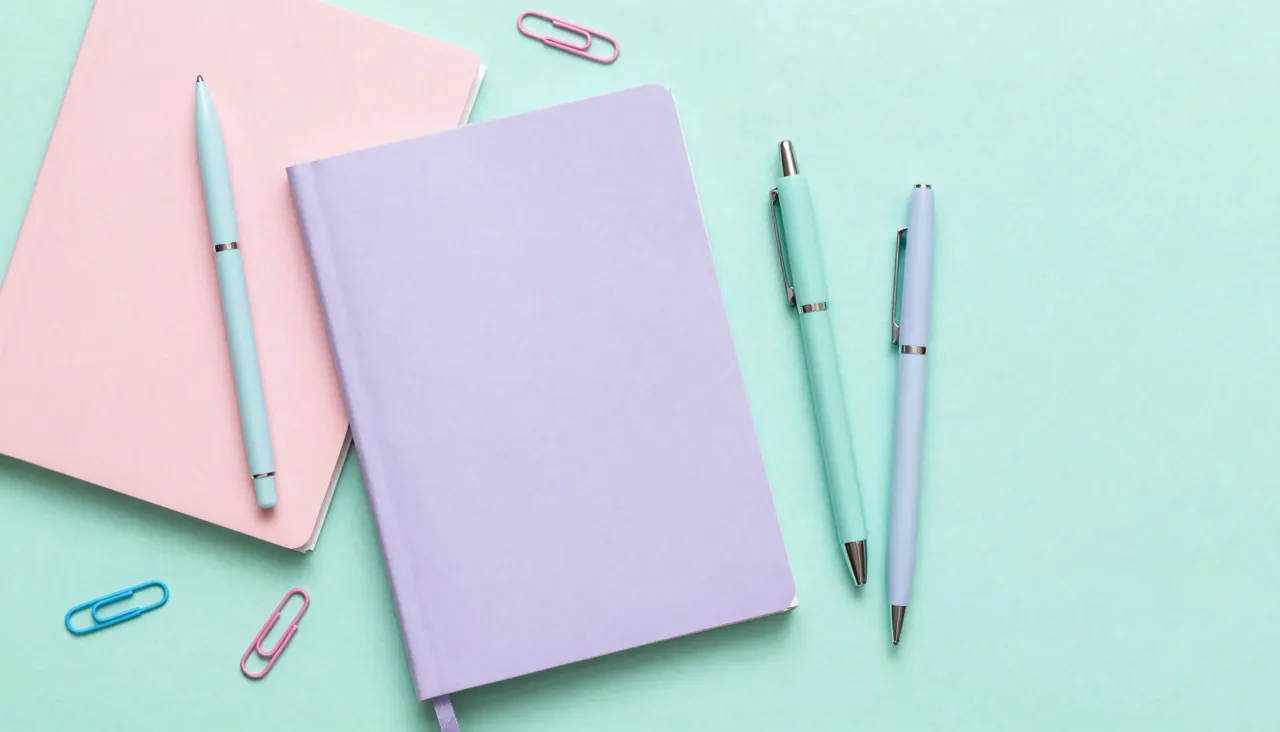 Cheerful flat lay of pastel notebooks, pens and clips on mint
