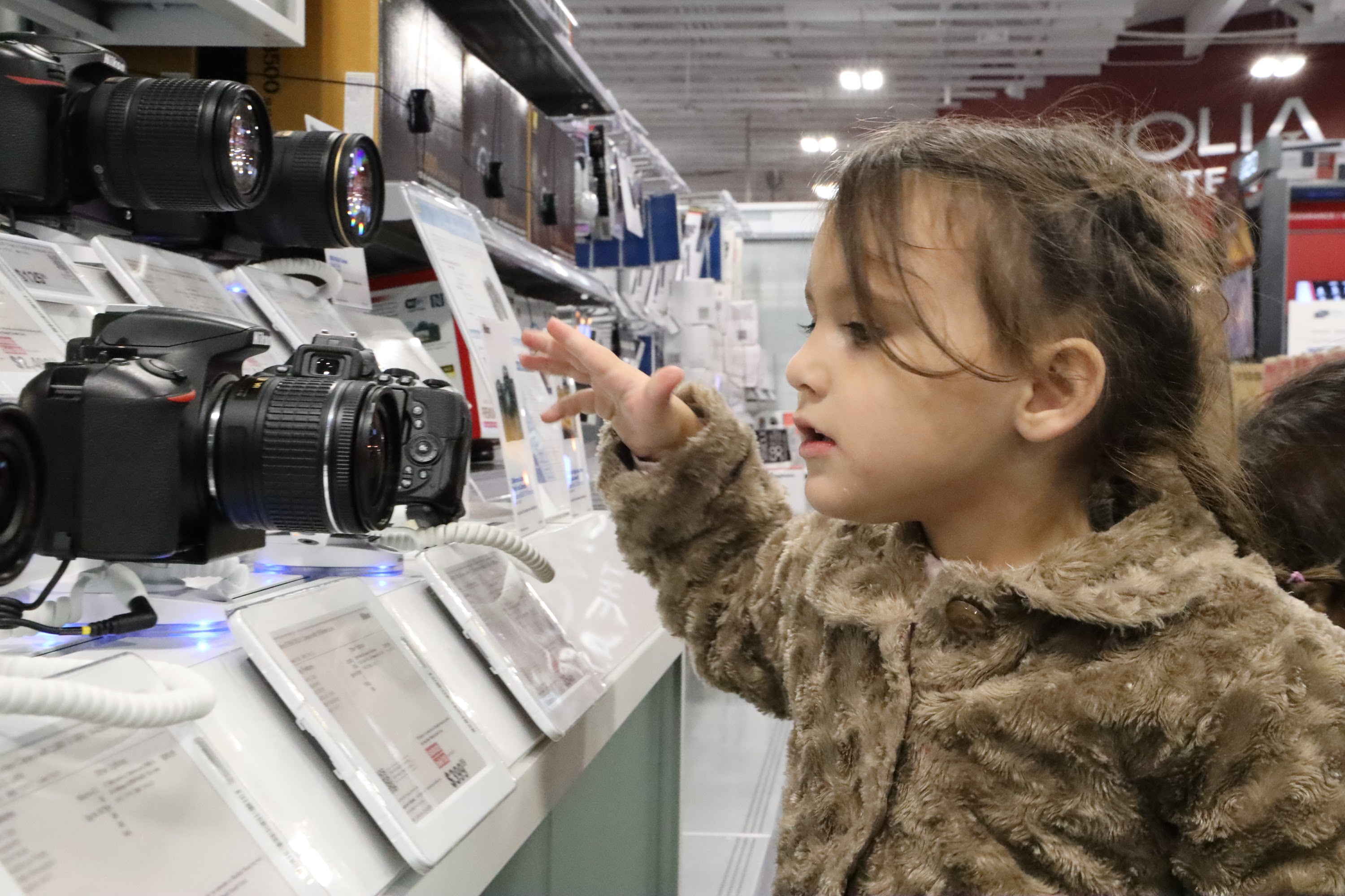 Young Girl Examining Cameras in Electronics Store