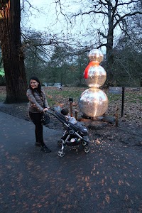 Woman Pushing Stroller Near Metallic Snowman Sculpture in Park