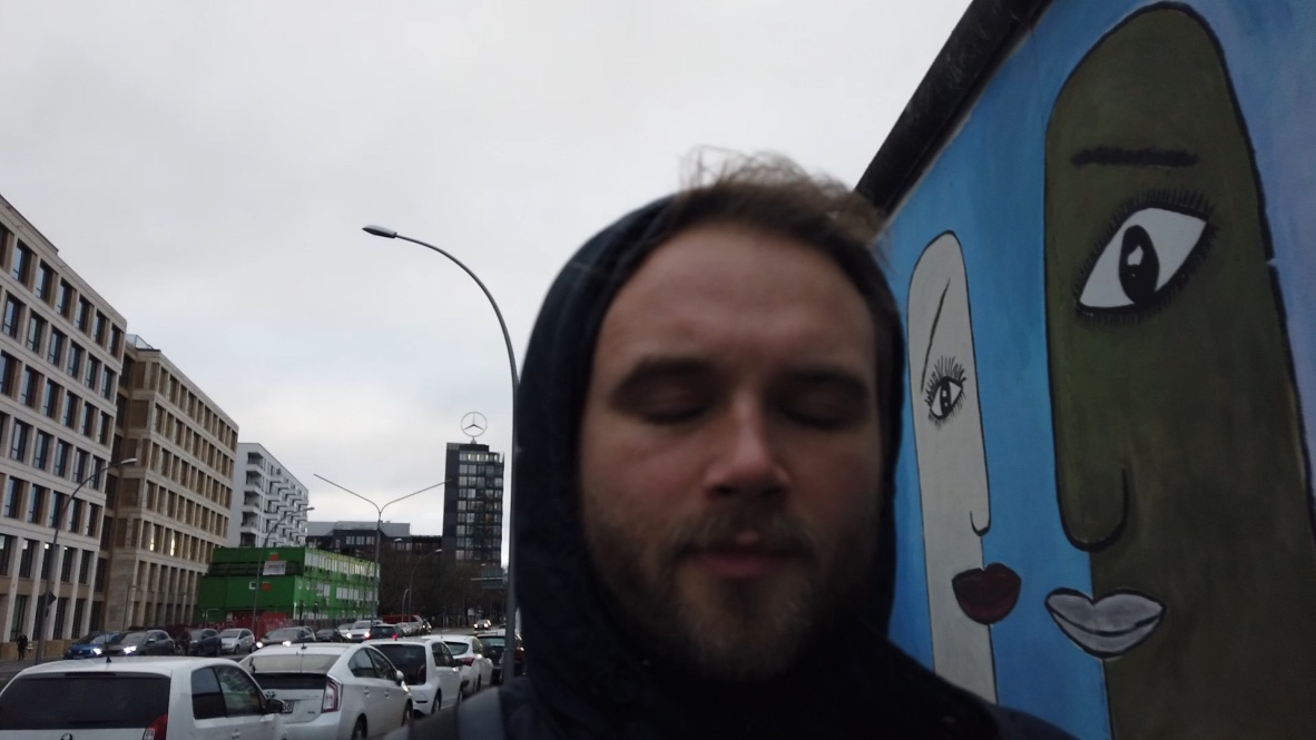Man in Hooded Jacket Standing Near Mural on Berlin Wall