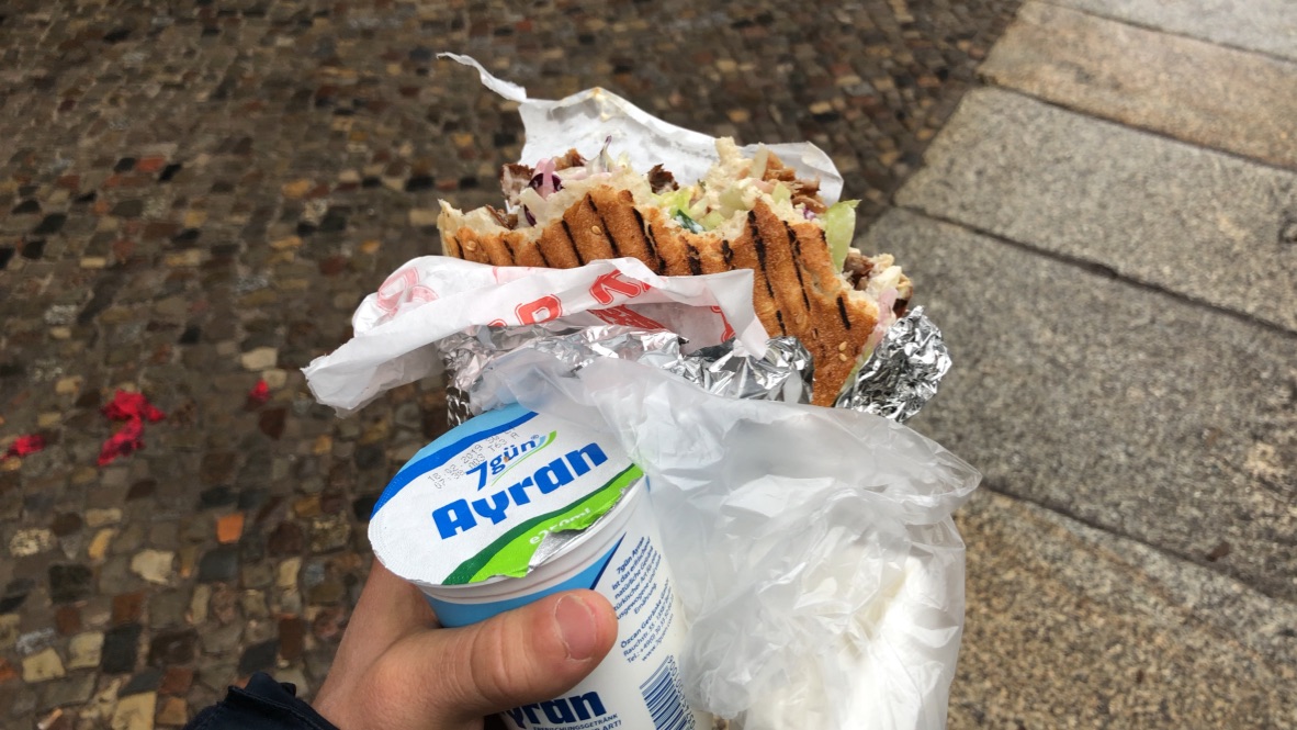 Hand Holding Ayran and Wrapped Sandwich on Cobblestone Street