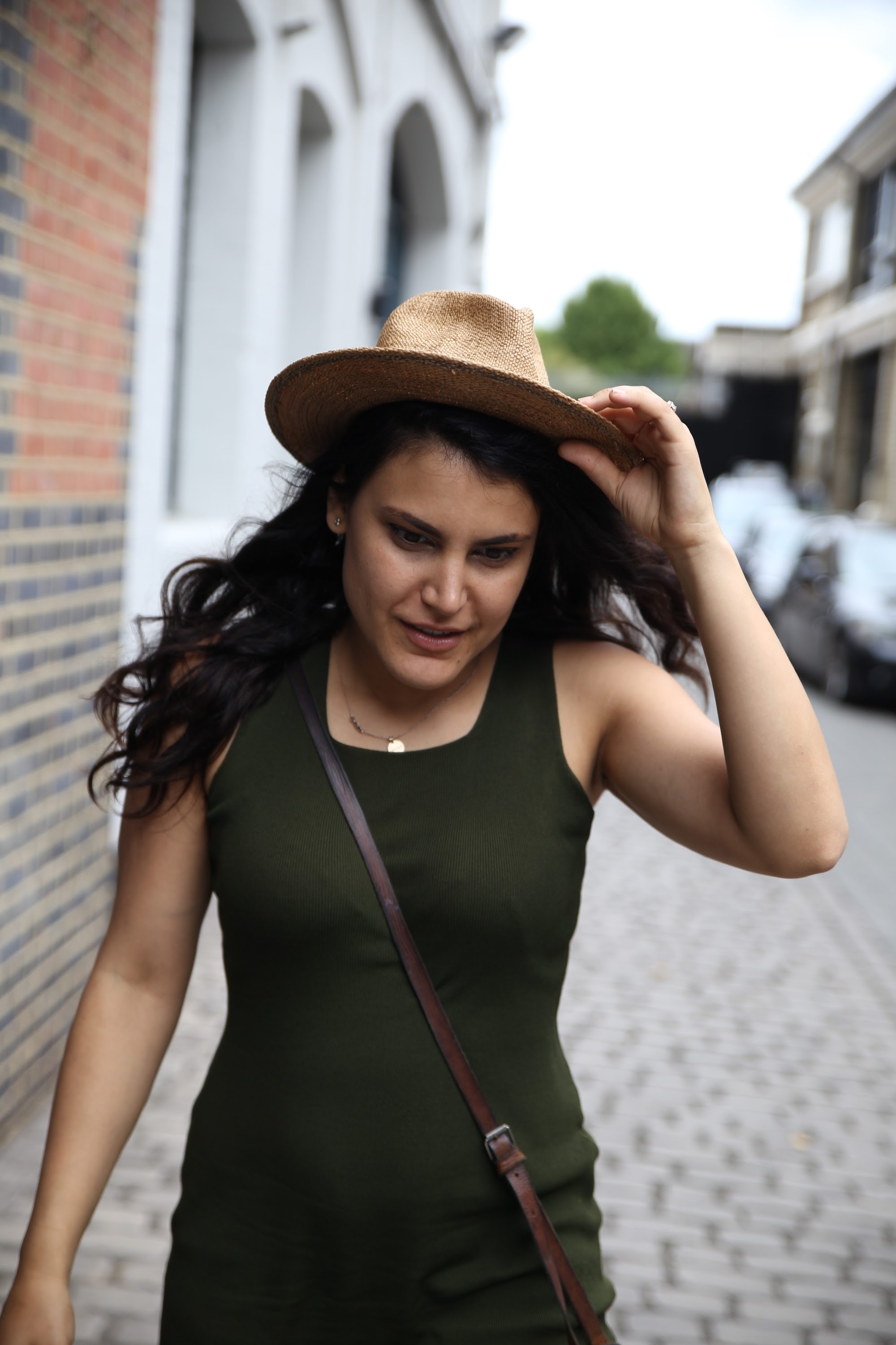 Woman Adjusting Straw Hat on Cobblestone Street