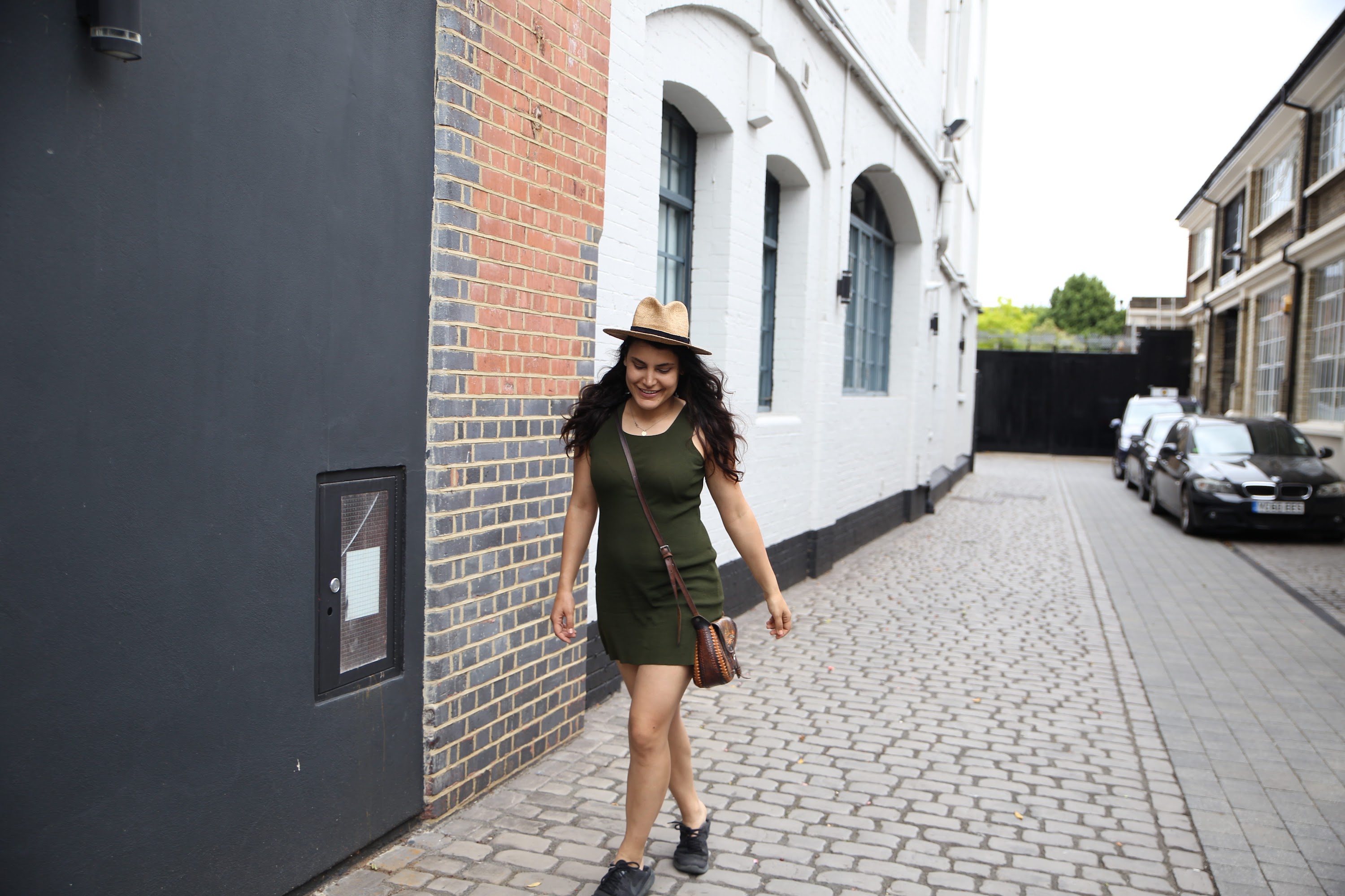 Woman Walking Down Cobblestone Alley in Green Dress and Hat