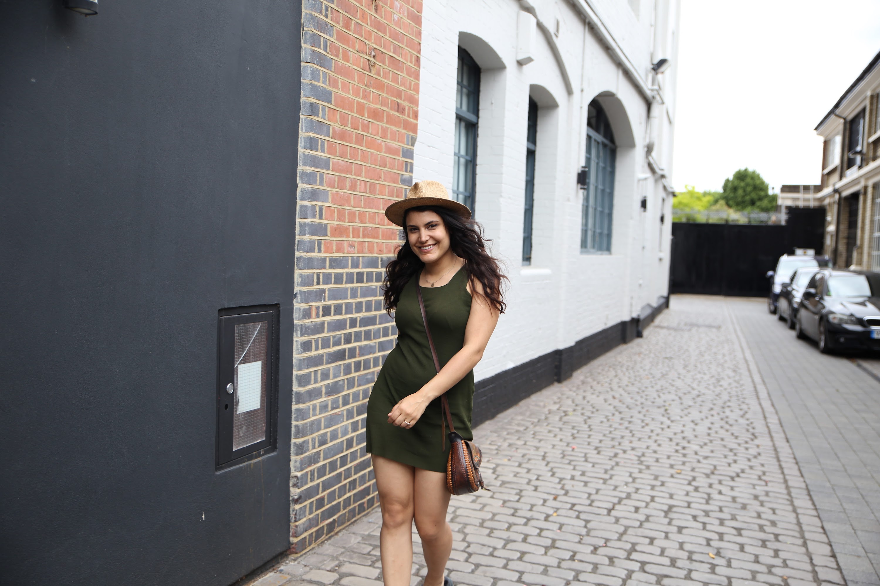 Woman in Green Dress and Hat Walking on Cobblestone Street