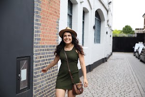 Woman in Green Dress and Fedora Hat Walking on Cobblestone Street
