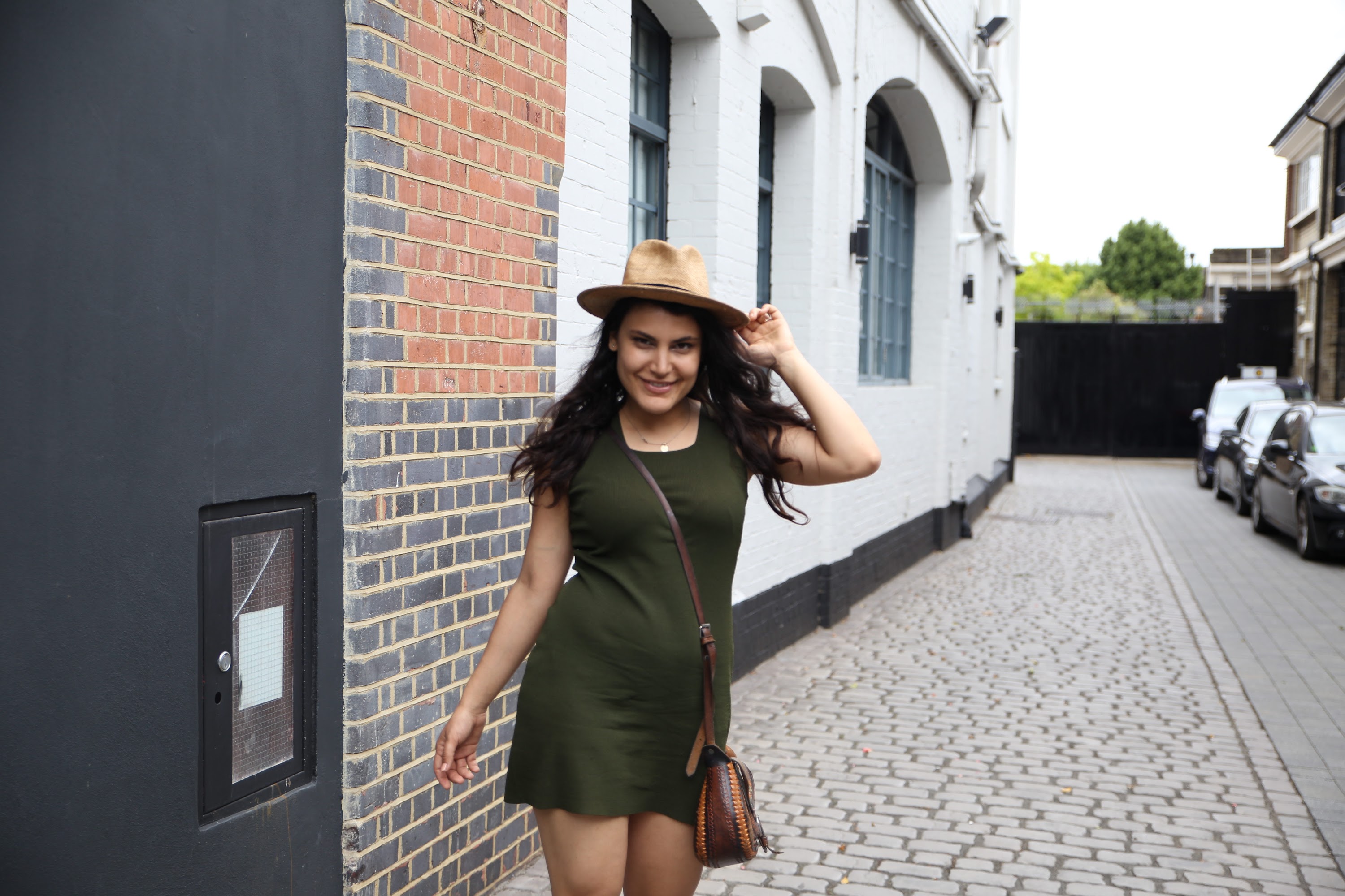 Woman in Green Dress and Fedora Hat on Cobblestone Street