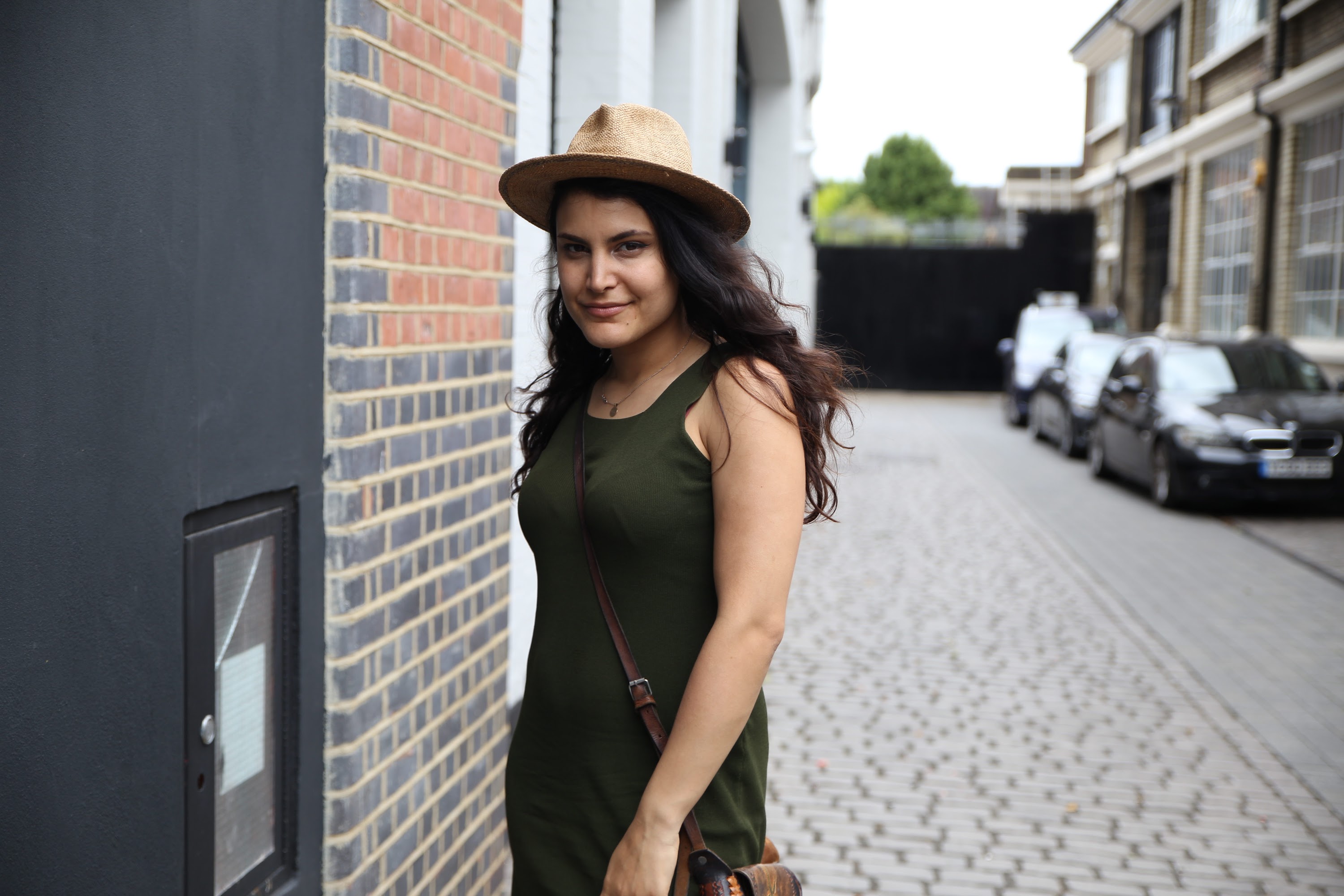 Woman in Hat and Green Dress Standing on Cobblestone Street