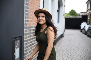 Woman in Green Dress and Straw Hat Walking Down a Cobblestone Alley