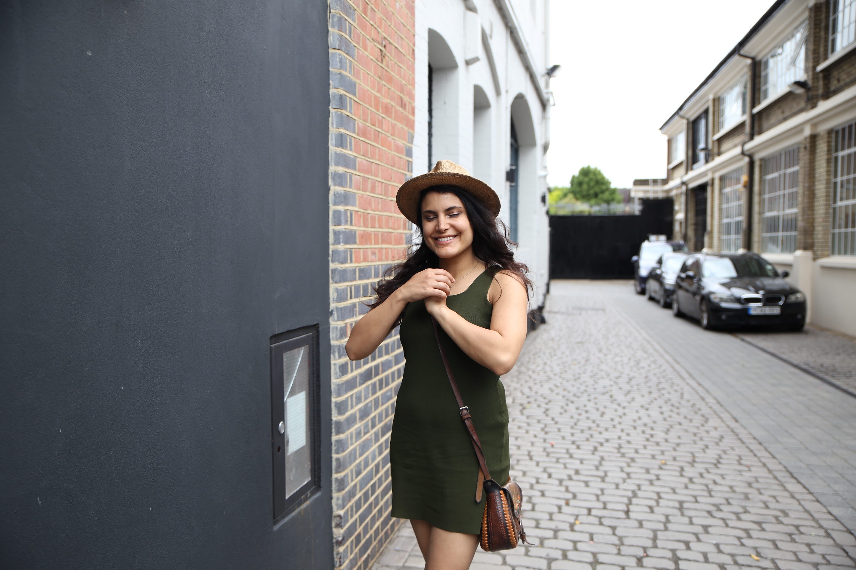 Woman in Green Dress and Hat Standing on Cobblestone Alley