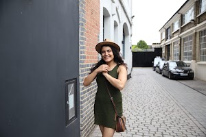 Woman in Green Dress and Hat Standing on Cobblestone Alley