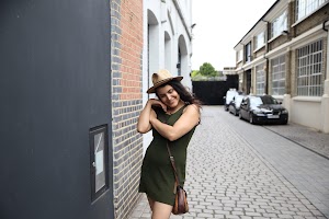 Woman in Green Dress and Fedora Hat Leaning Against Brick Wall