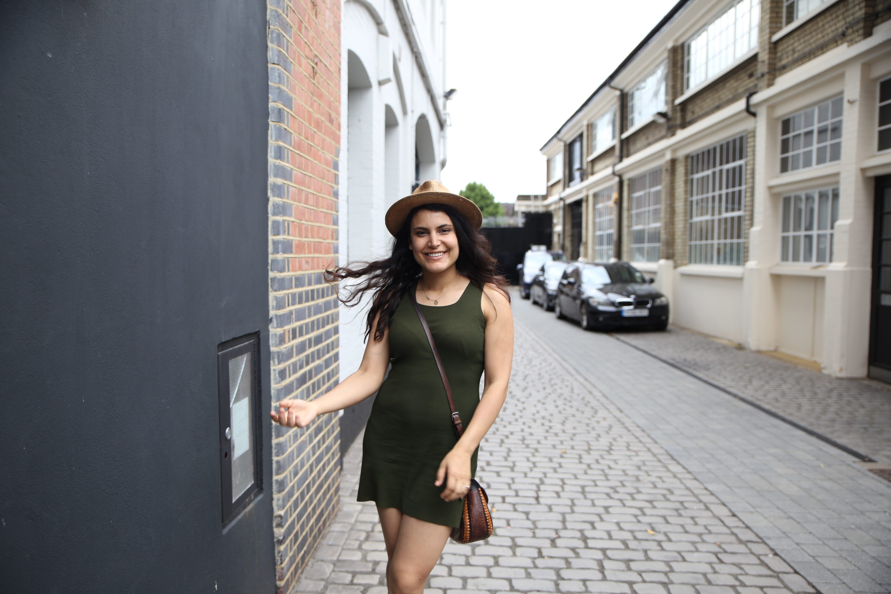 Woman in Green Dress and Hat Walking Down Cobblestone Alley