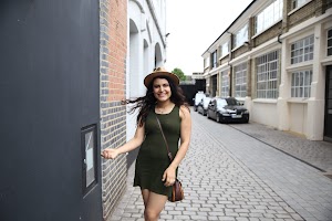 Woman in Green Dress and Hat Walking Down Cobblestone Alley