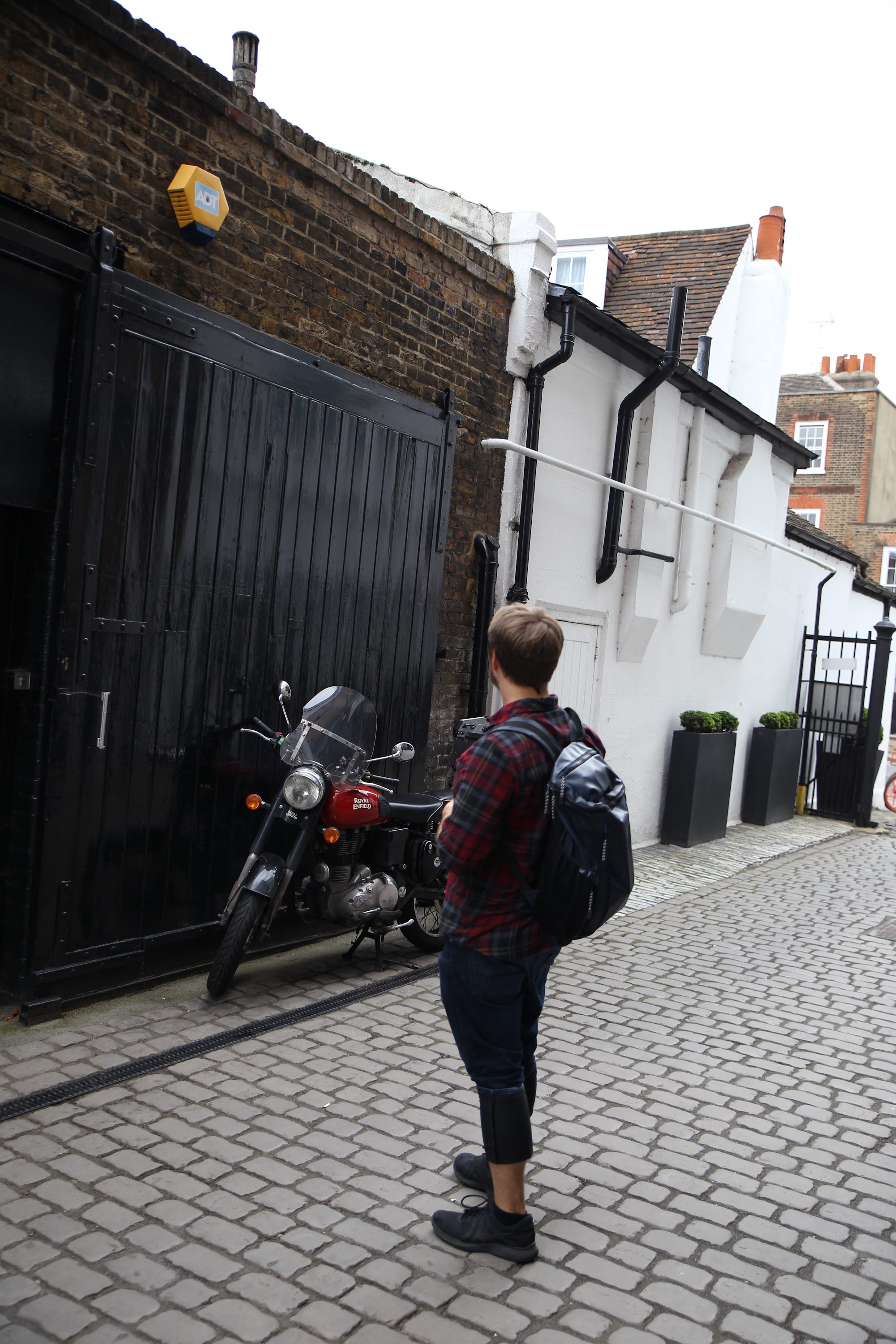 Man Standing in Cobblestone Alley with Red Motorcycle