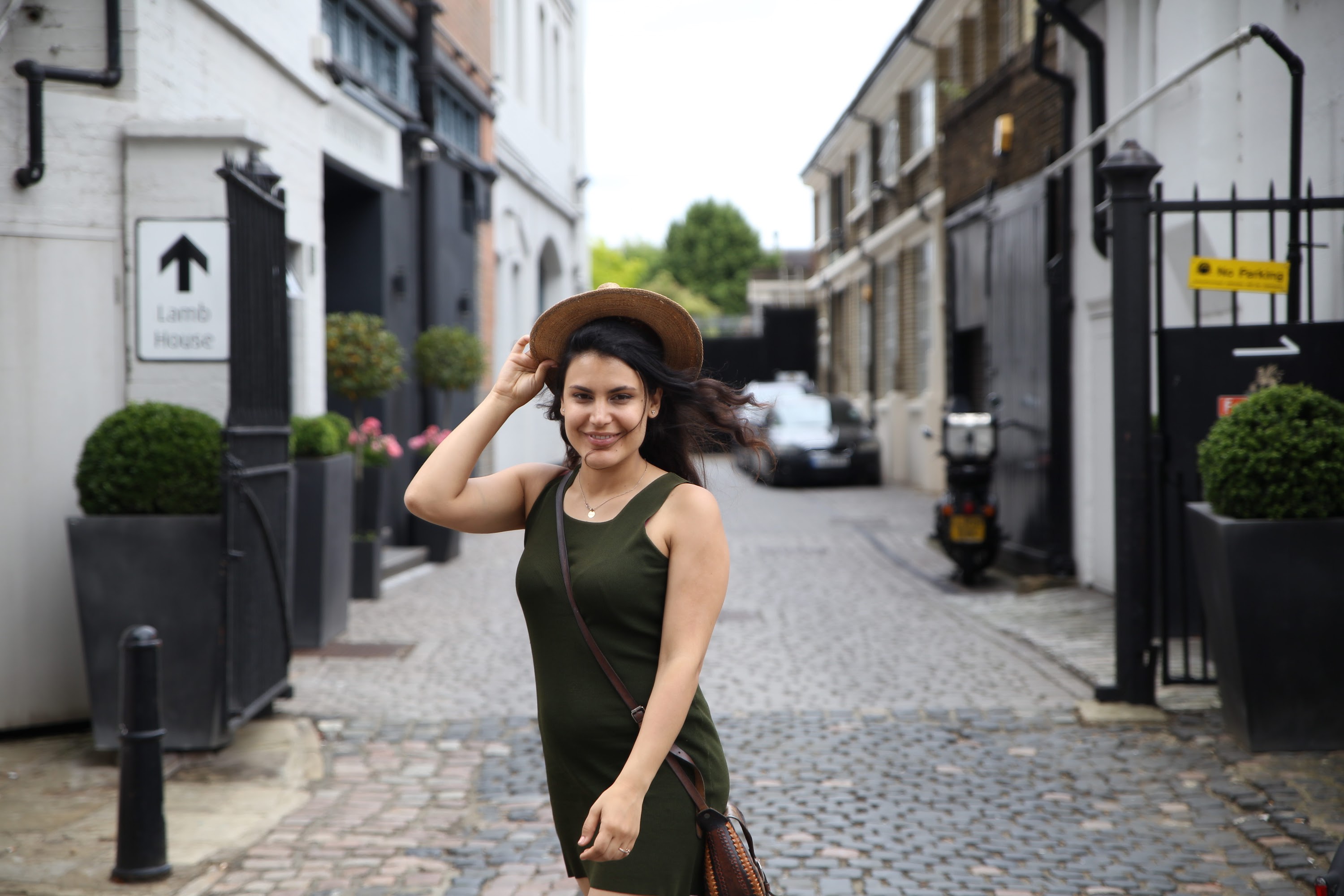 Woman in Green Dress and Brown Hat on Cobblestone Alley