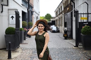 Woman in Green Dress and Brown Hat on Cobblestone Alley