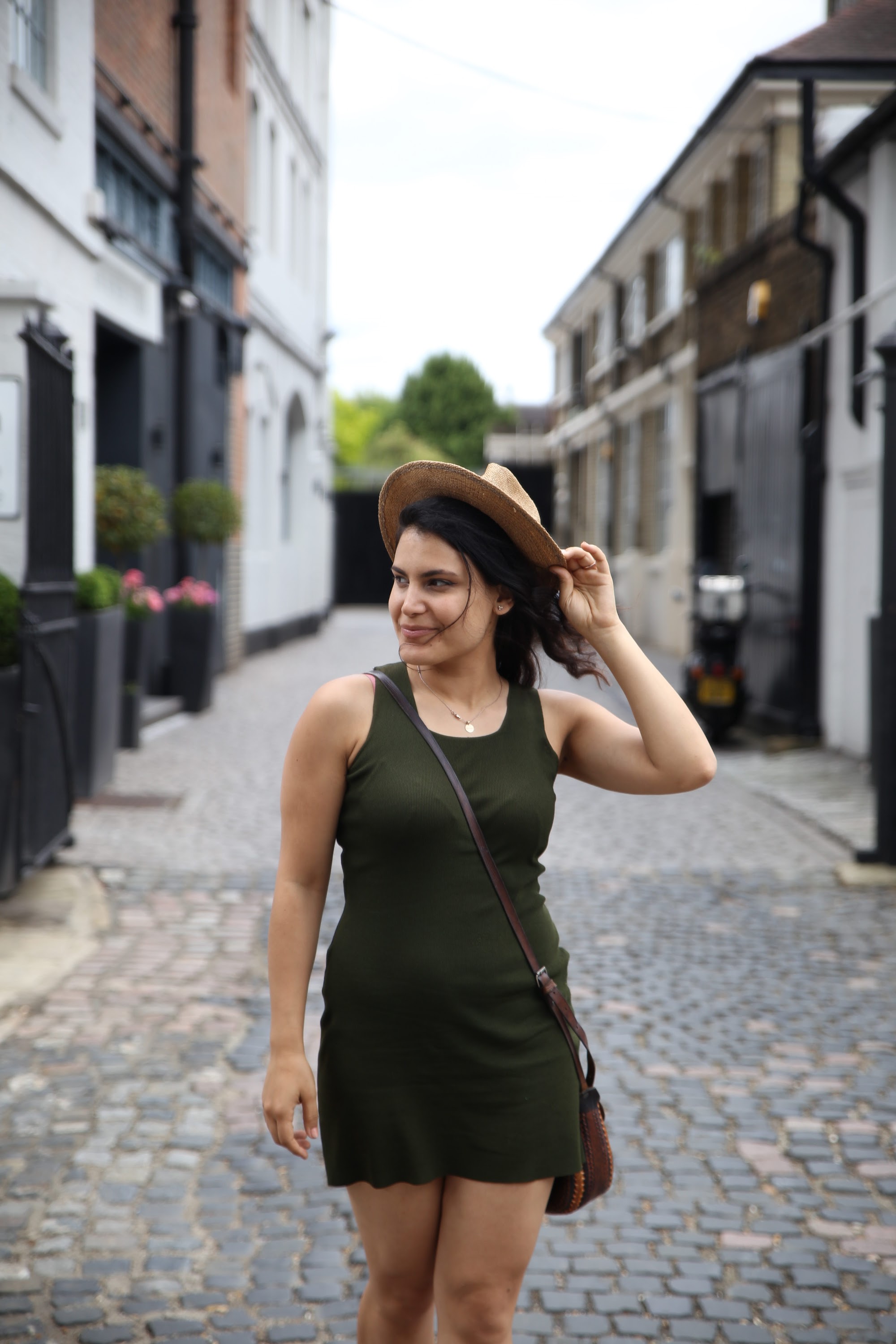 Woman in Green Dress Holding Straw Hat on Cobblestone Street