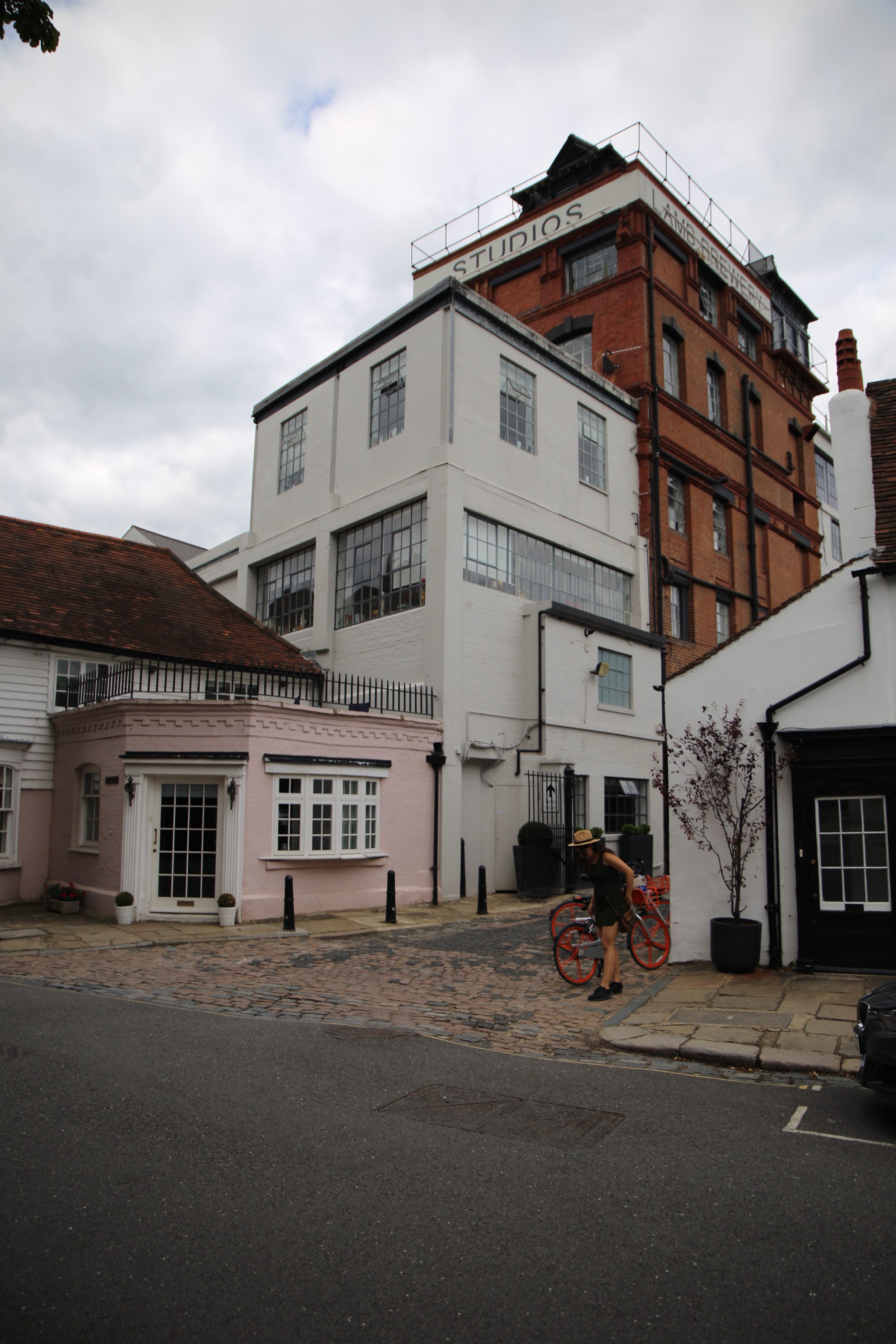 Person with Red Bicycle on Cobblestone Street Near Studios Building