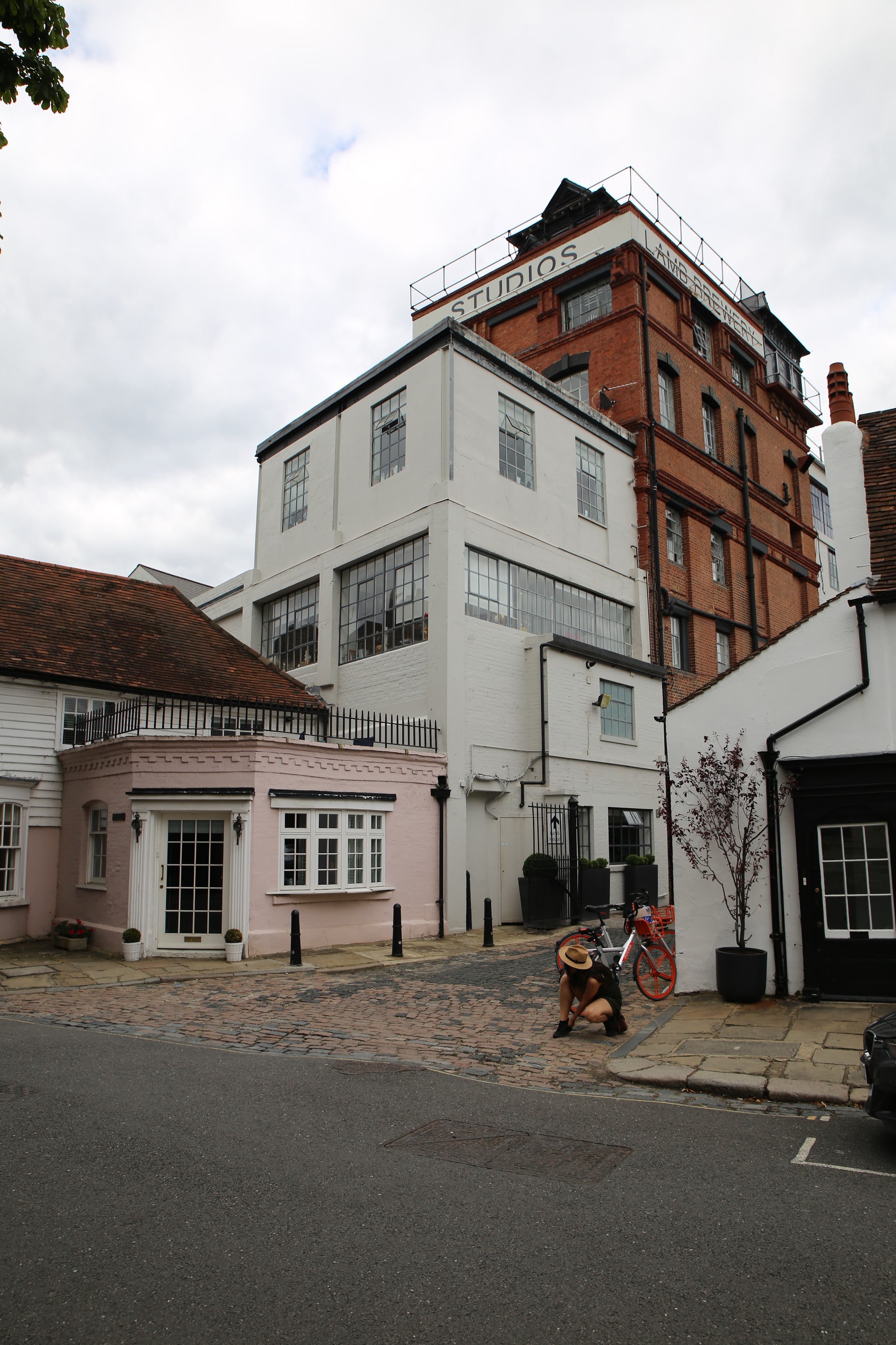 Person Crouching Near Red Bicycle in Front of White and Brick Studios Building