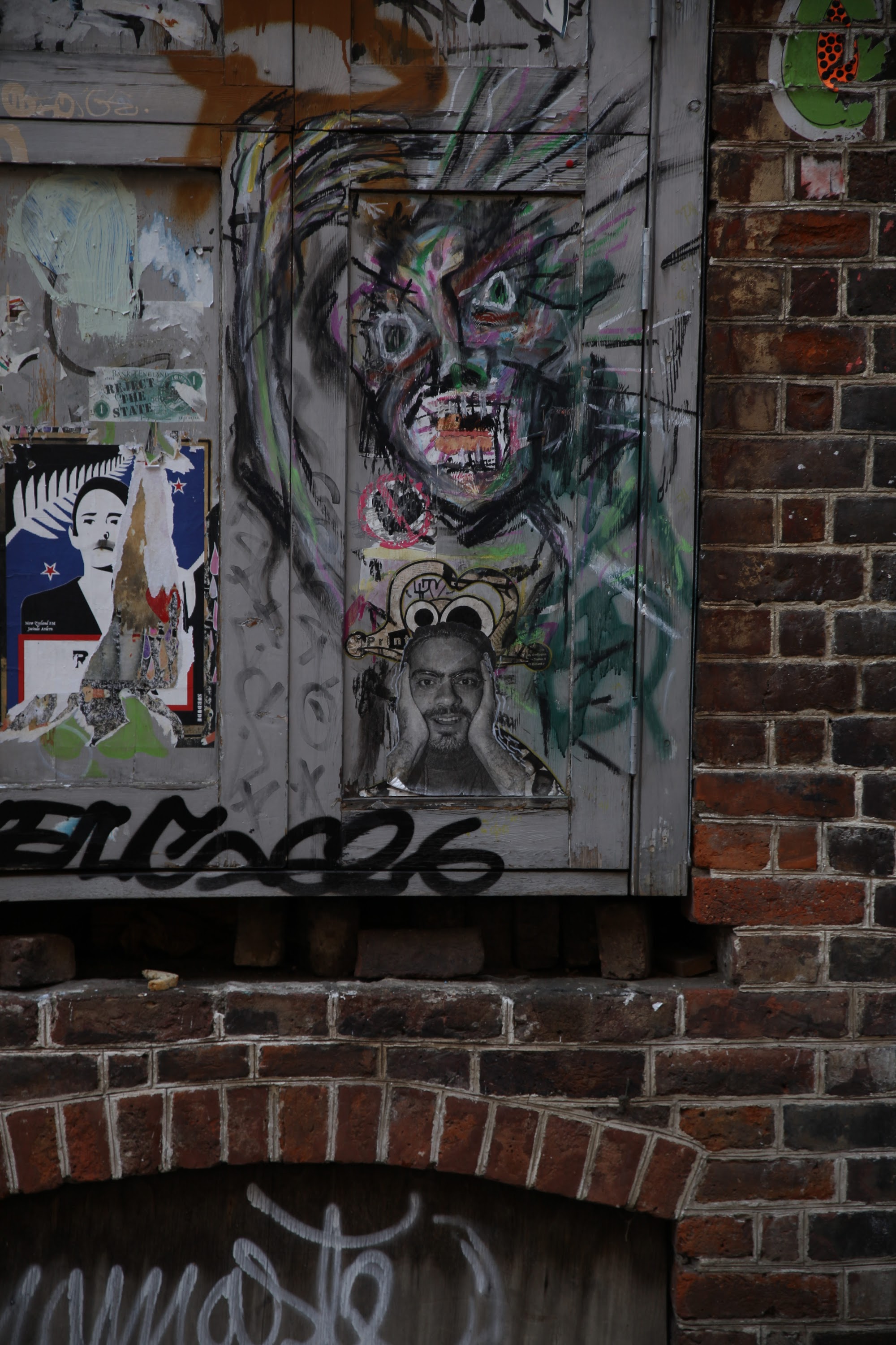 Graffiti-covered door with layered street art and brick wall