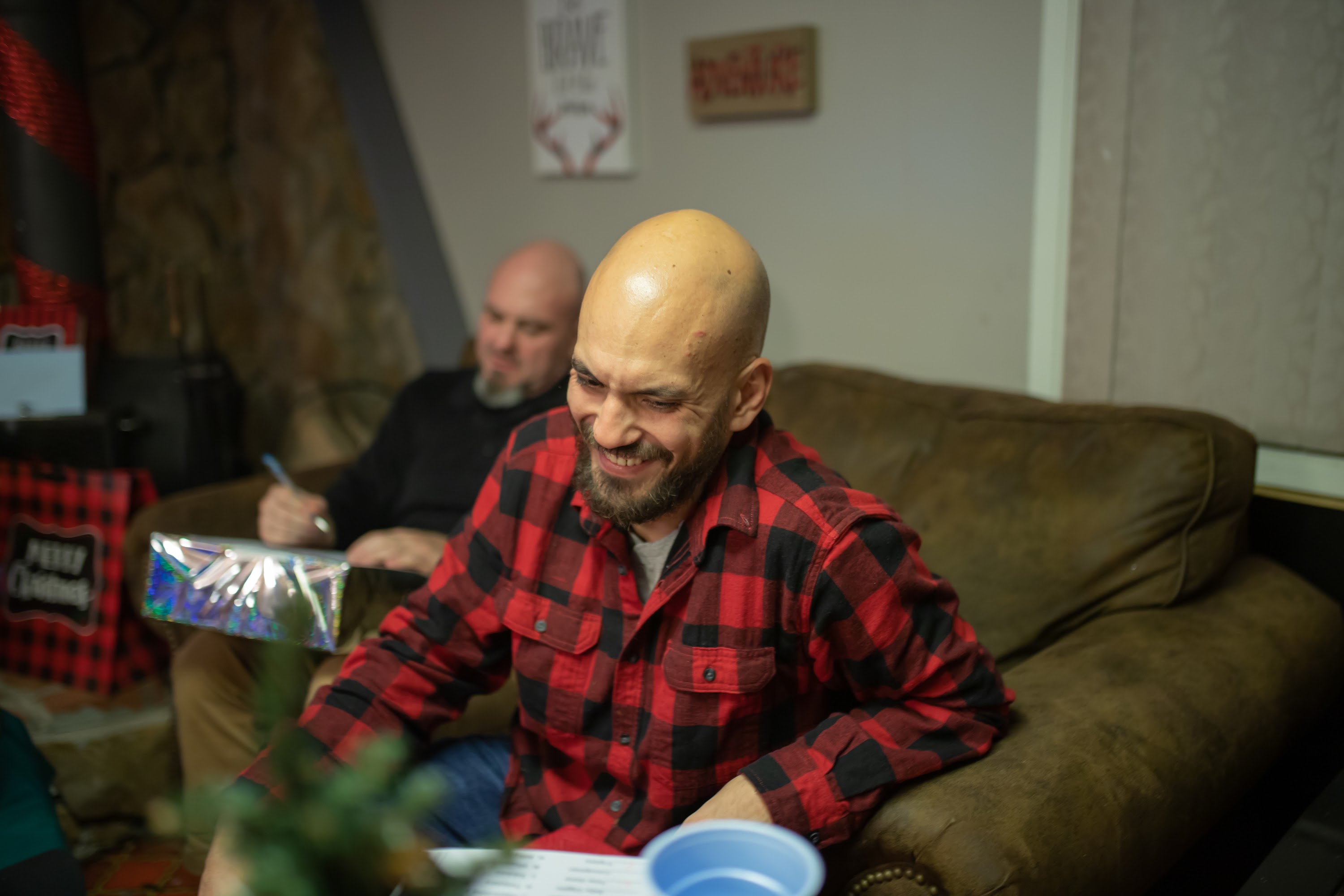 Man in Red Plaid Shirt Laughing While Sitting on Couch
