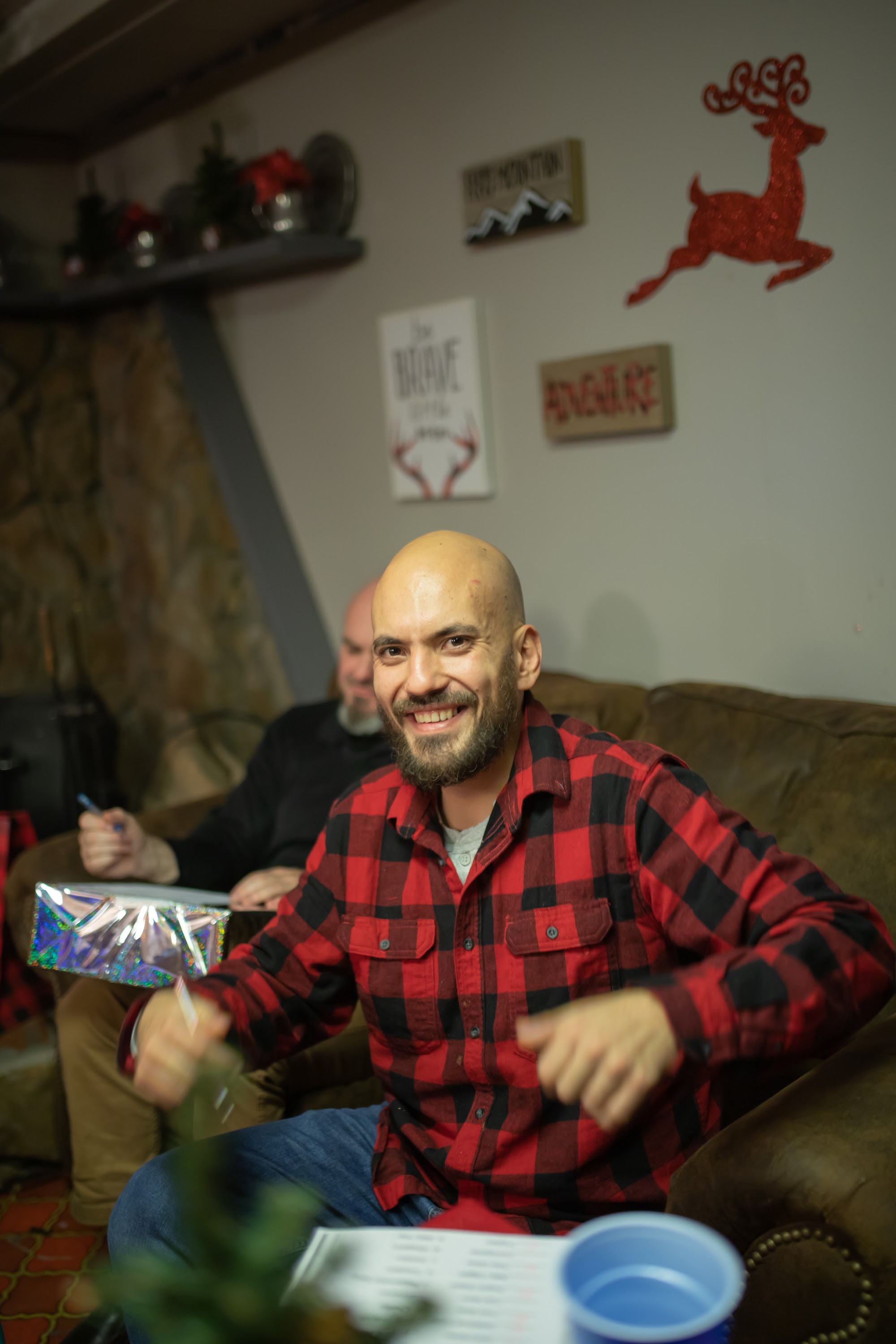 Bald man in red plaid shirt smiling while opening gift