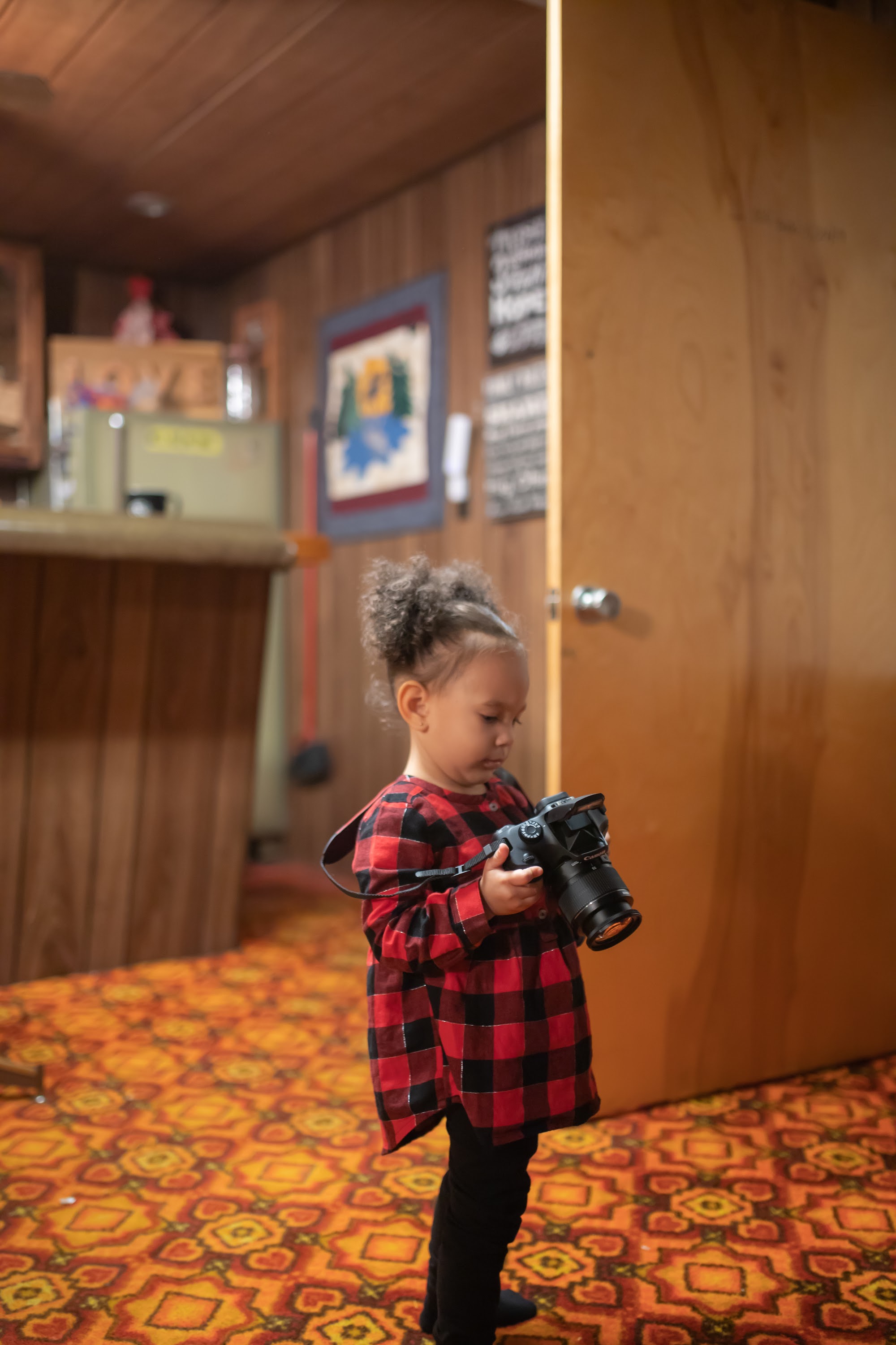 Toddler Holding Camera in Wood-Paneled Room
