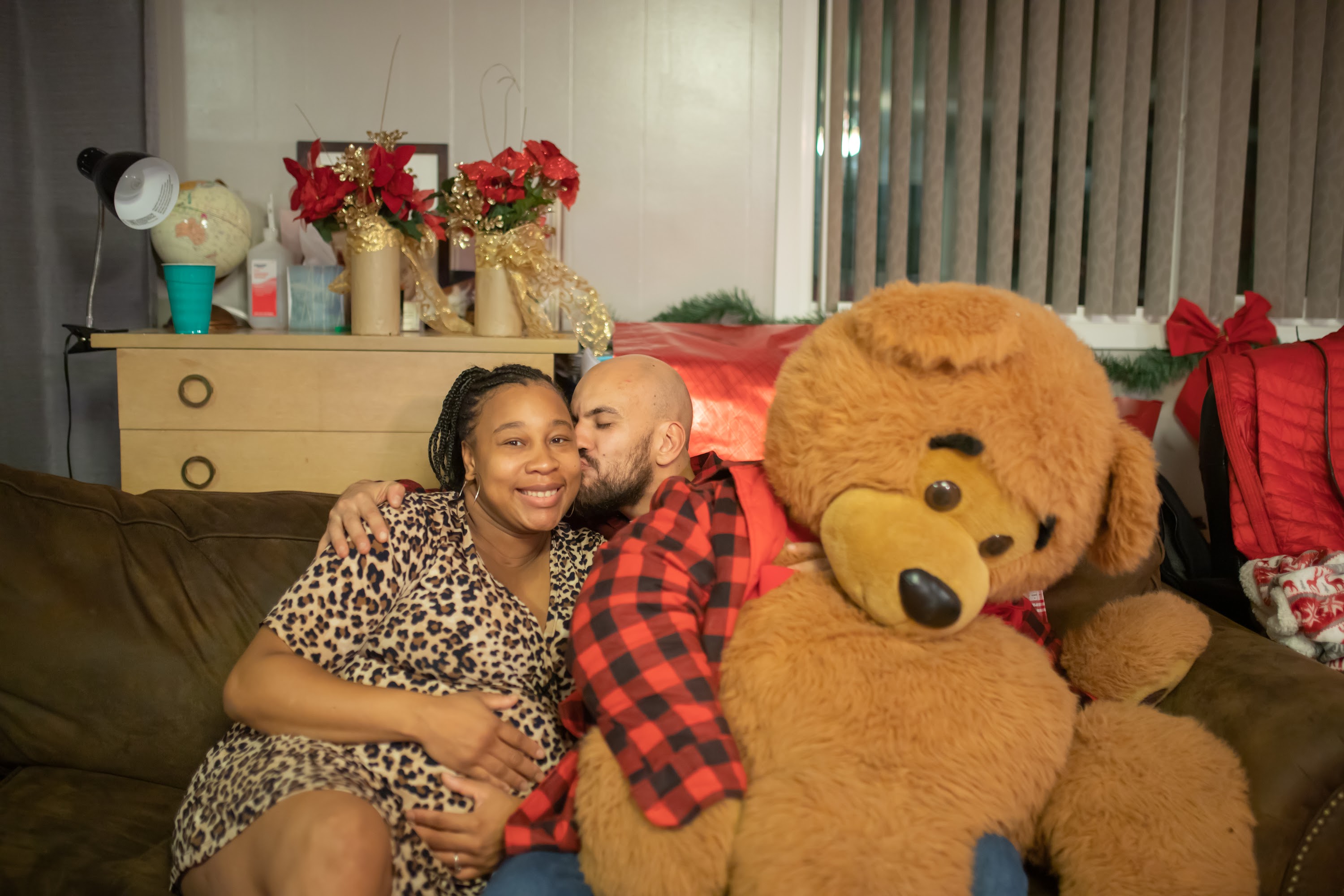 Pregnant Woman and Partner Sharing a Kiss with Giant Teddy Bear