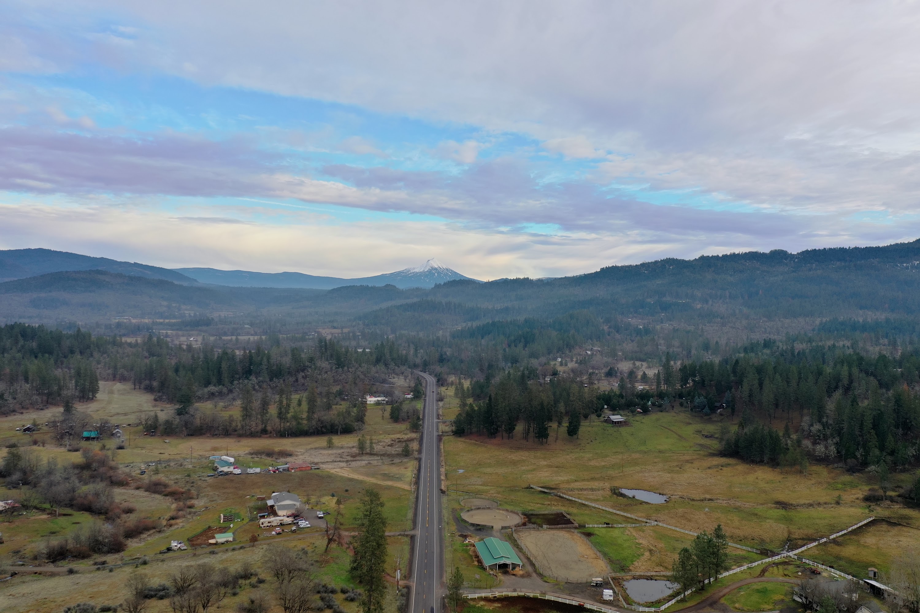 Aerial View of Rural Highway Through Forested Hills with Distant Snow-Capped Mountain