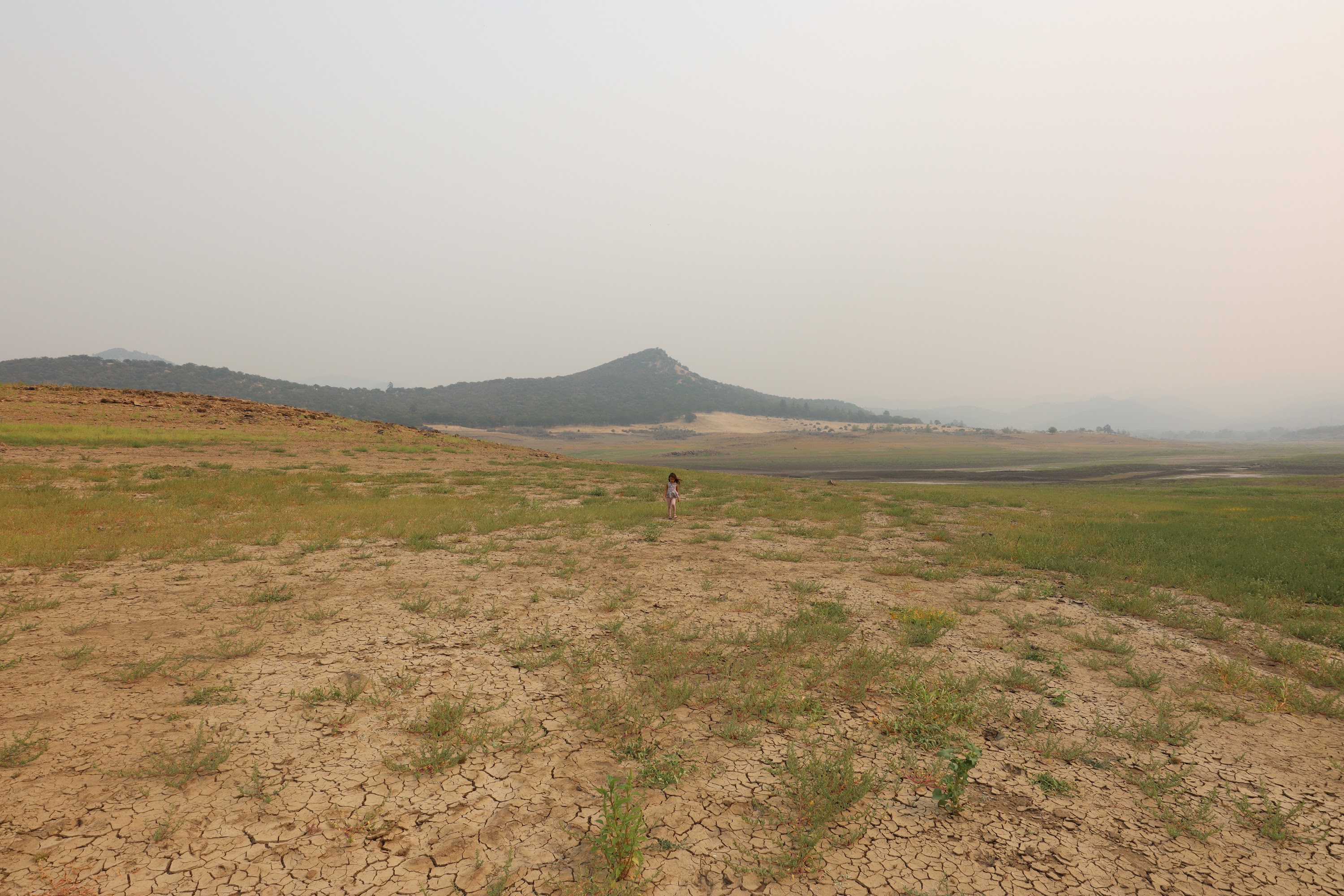 Child Standing in Cracked, Dry Landscape with Distant Hills