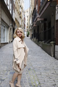 Blonde Woman in Beige Trench Coat on Cobblestone Alley