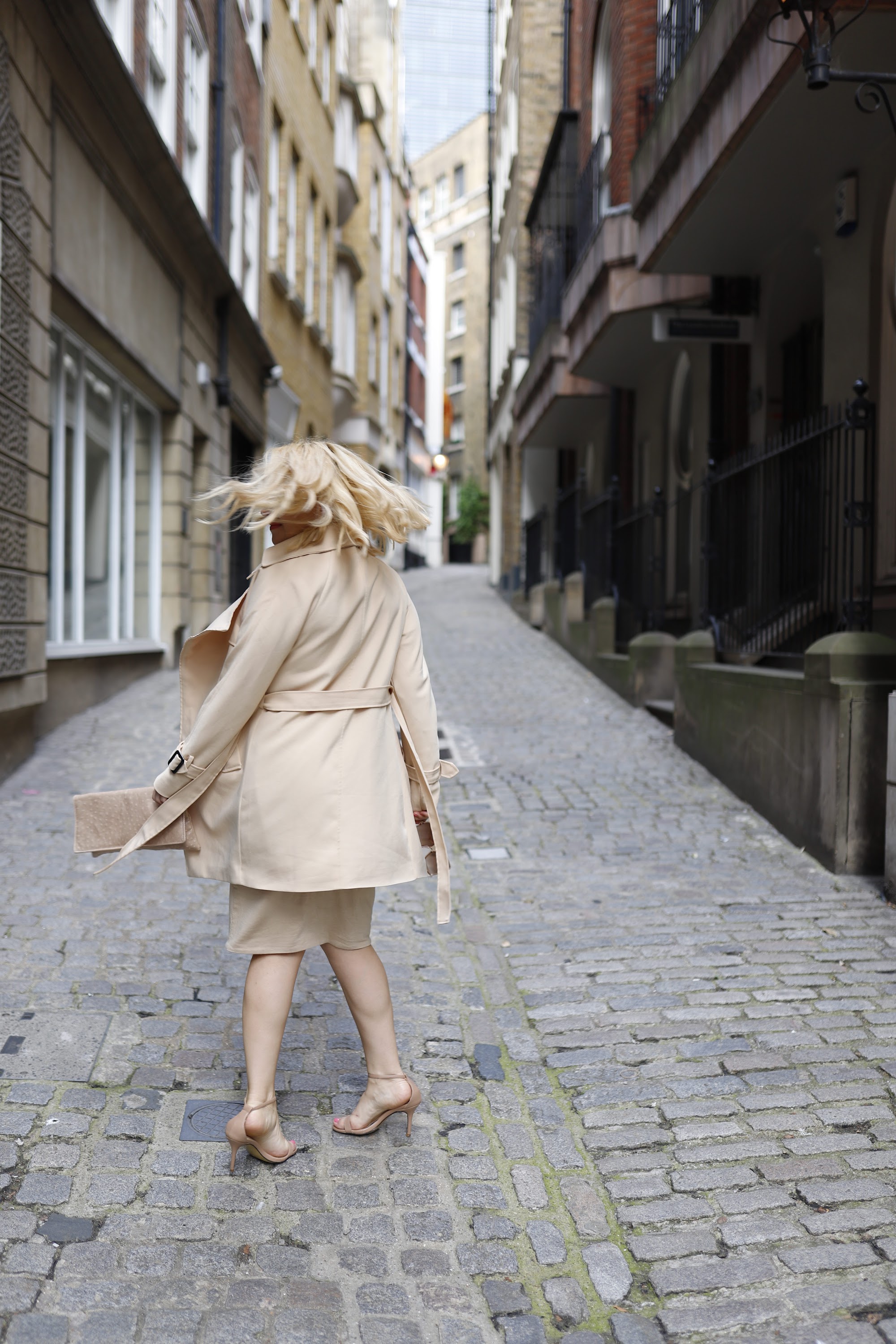 Blonde Woman in Beige Trench Coat on Cobblestone Alley