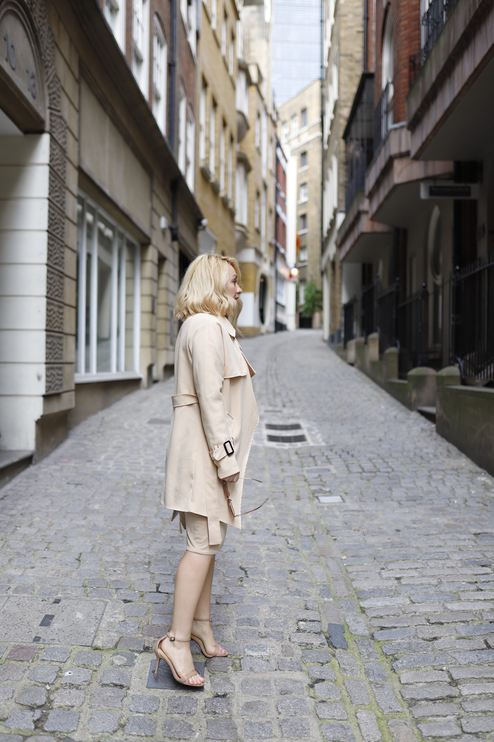 Blonde Woman in Beige Trench Coat on Cobblestone Alley