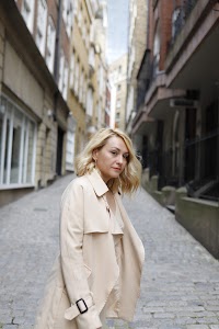 Blonde Woman in Beige Trench Coat on Cobblestone Alley