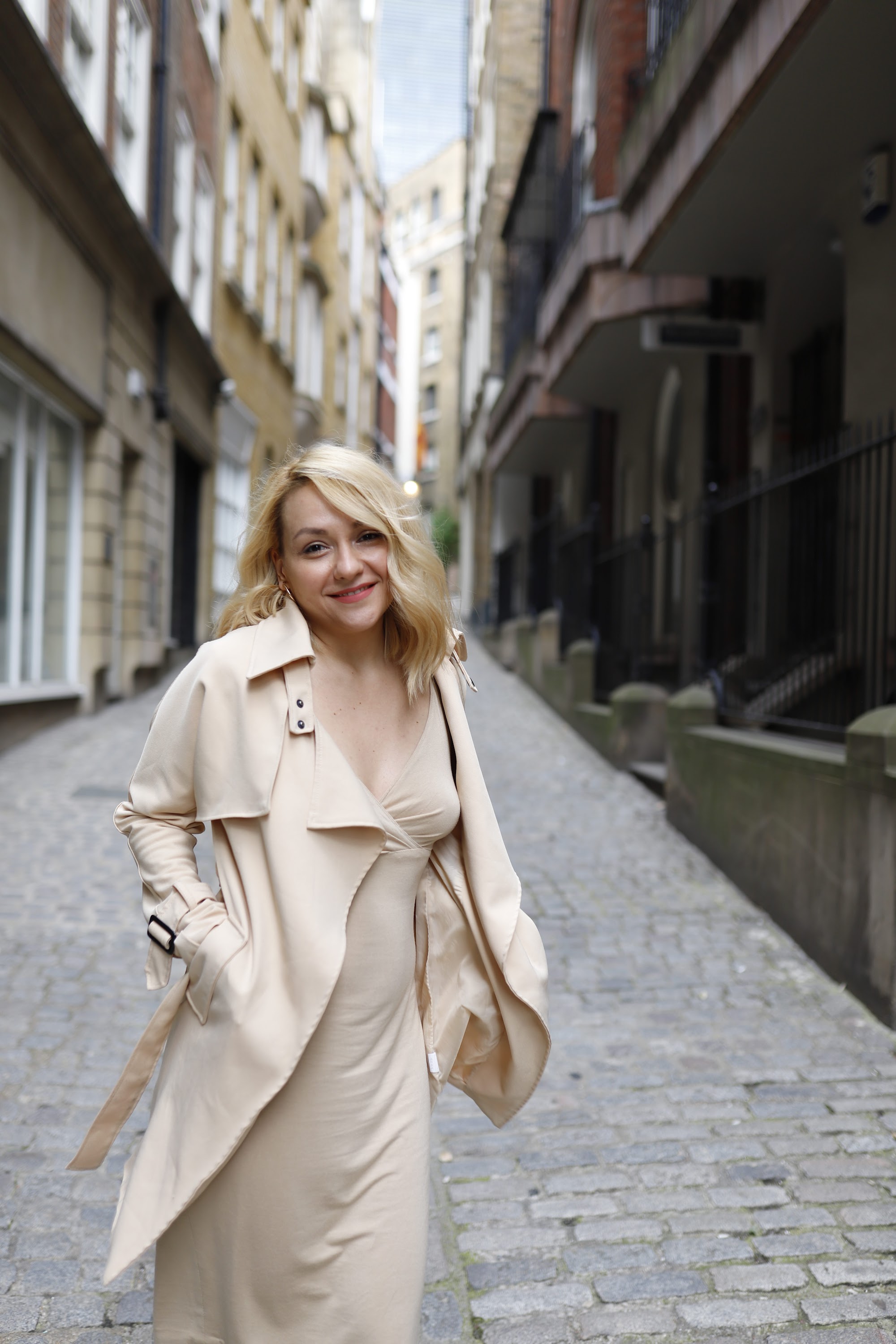 Blonde Woman in Beige Trench Coat on Cobblestone Alley