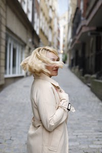Blonde Woman in Beige Trench Coat on Cobblestone Alley