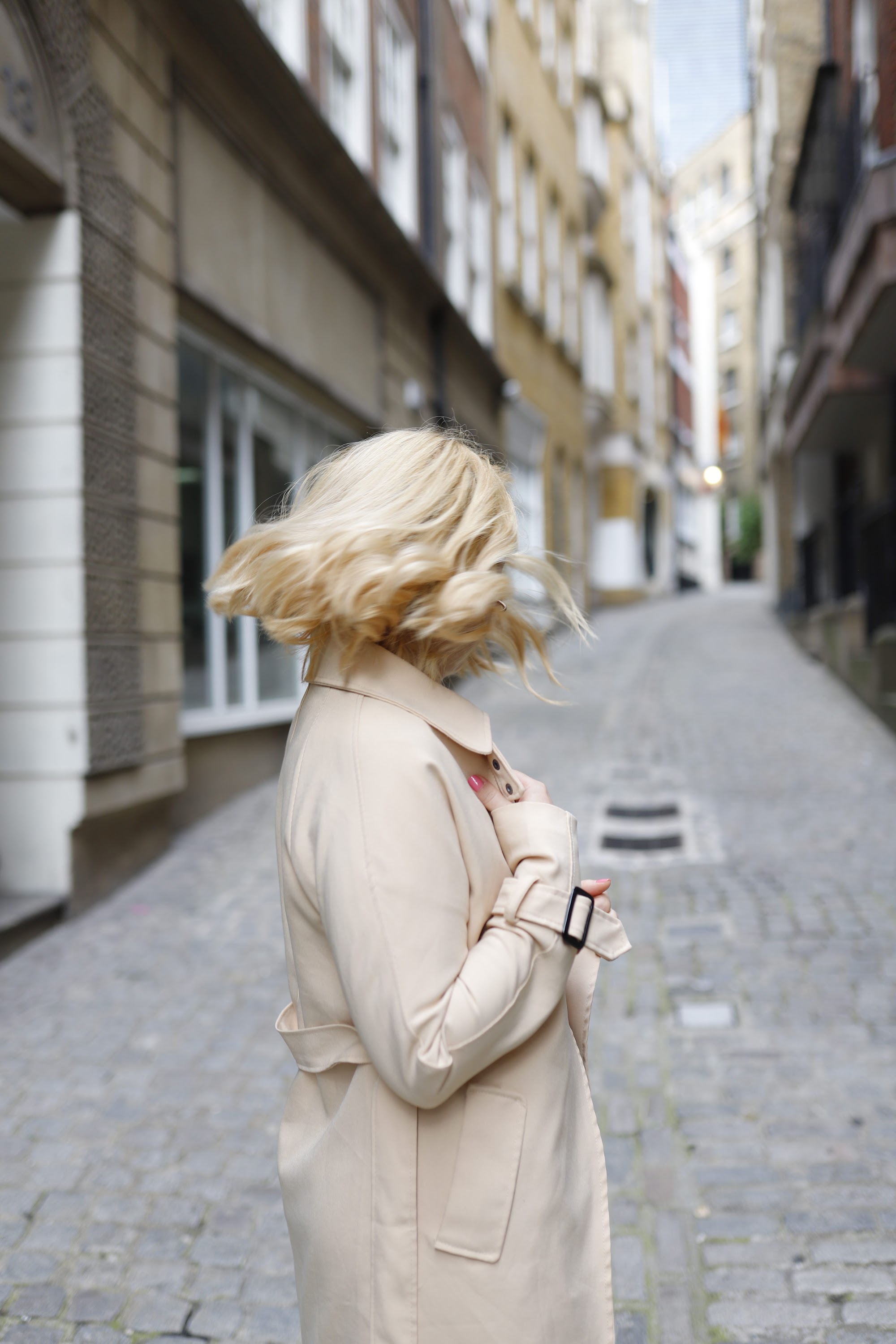 Blonde Woman in Beige Trench Coat on Cobblestone Alley