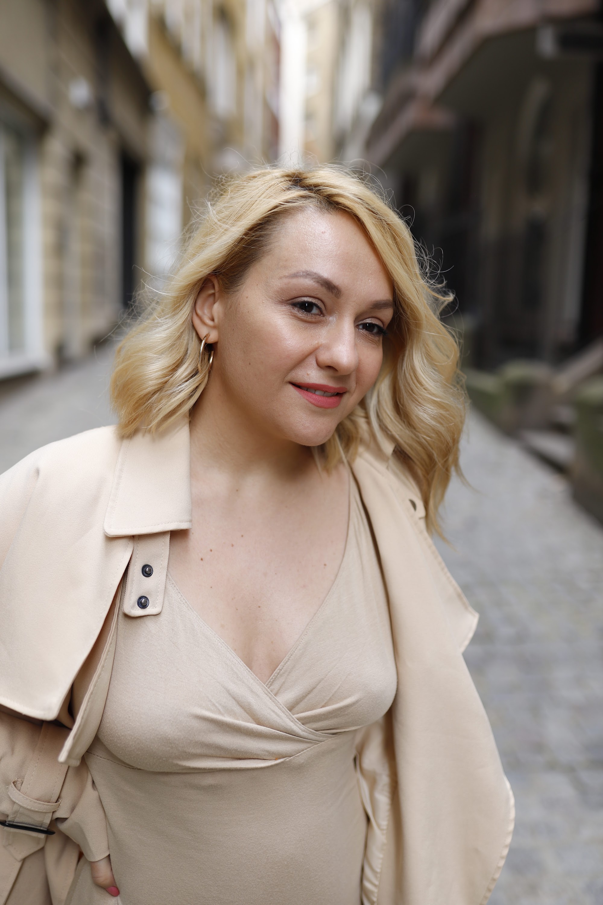 Blonde Woman in Beige Trench Coat on Cobblestone Alley