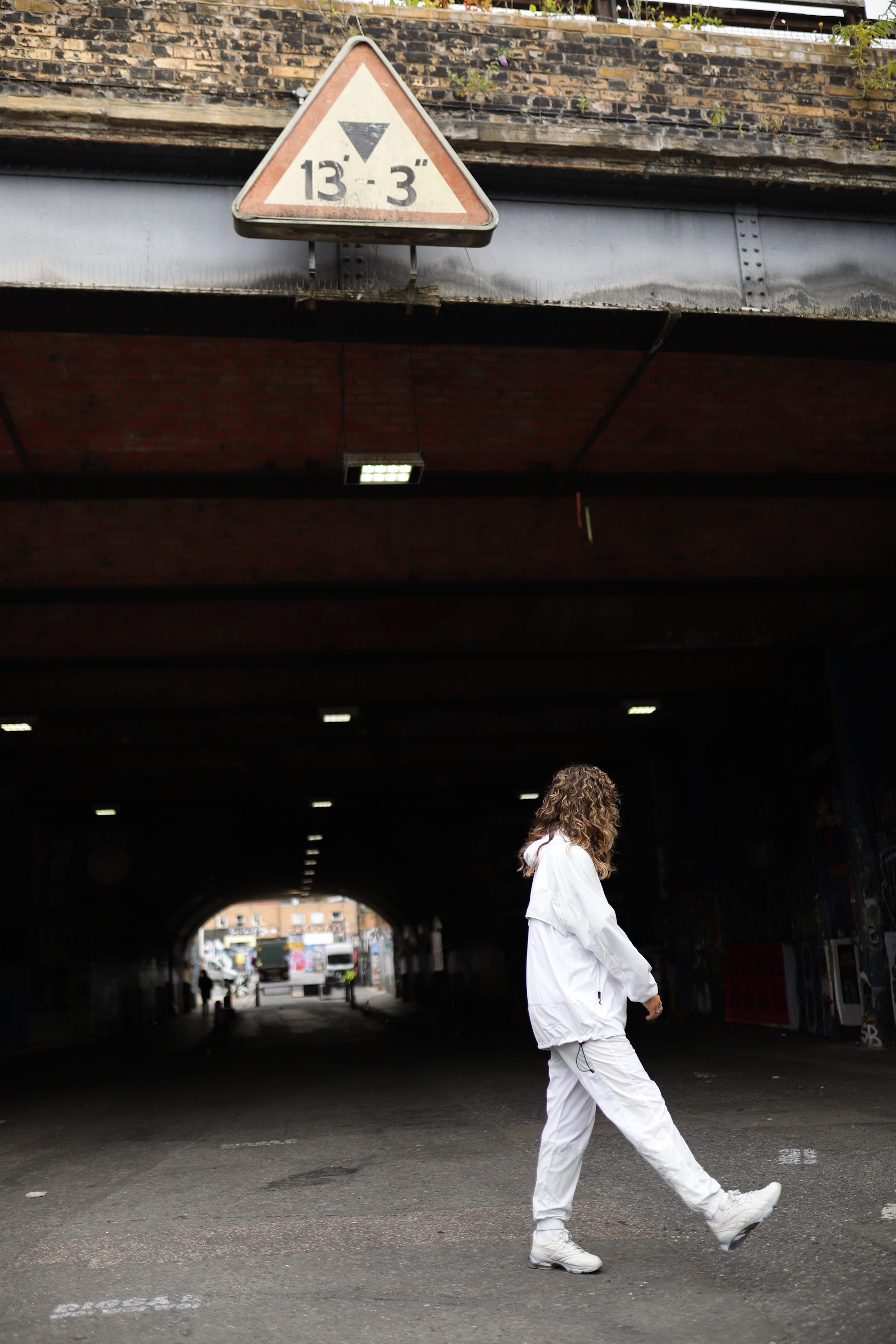 Woman in White Jacket Holding Sunglasses – Dark Urban Tunnel