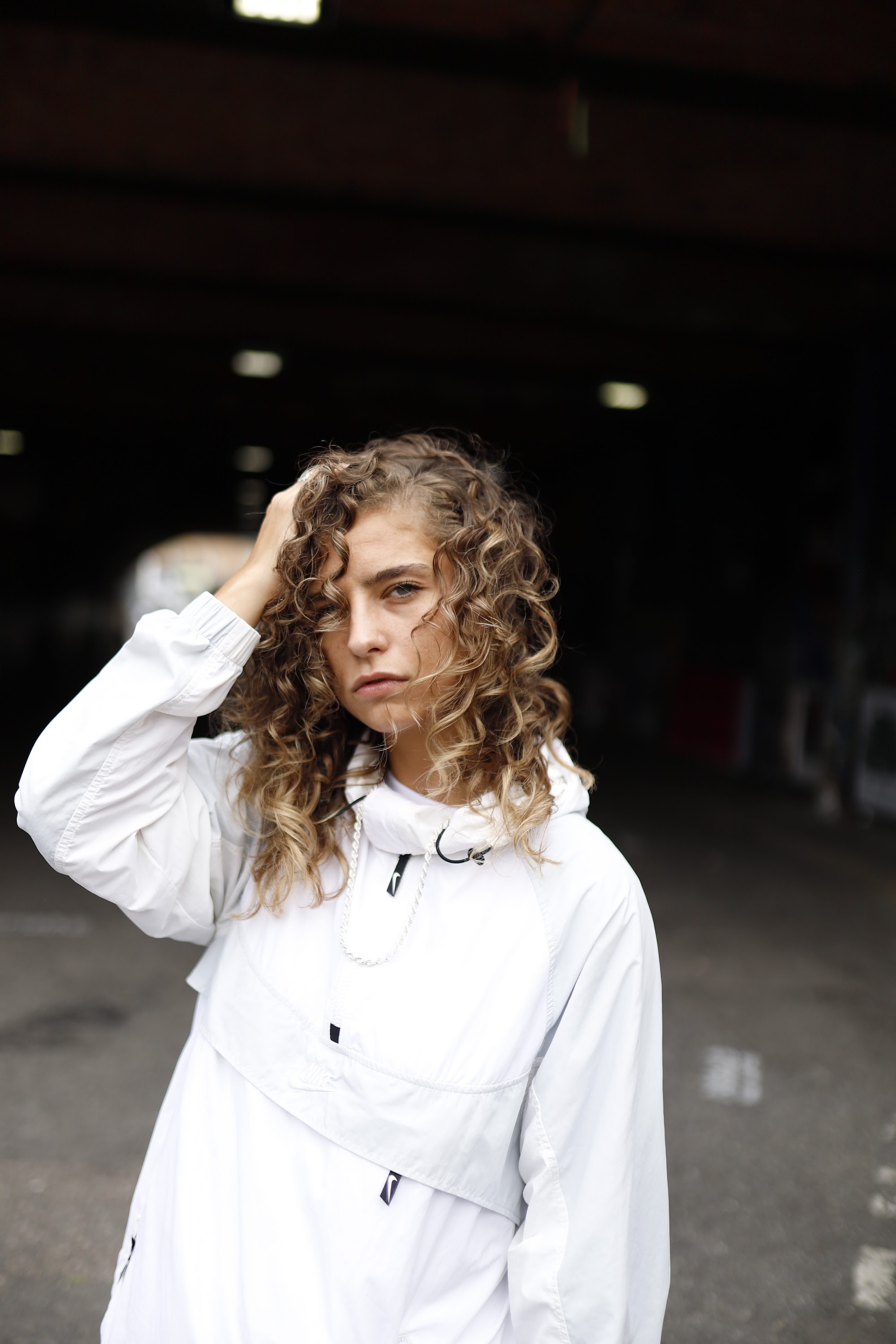 Woman in White Jacket Holding Sunglasses – Dark Urban Tunnel