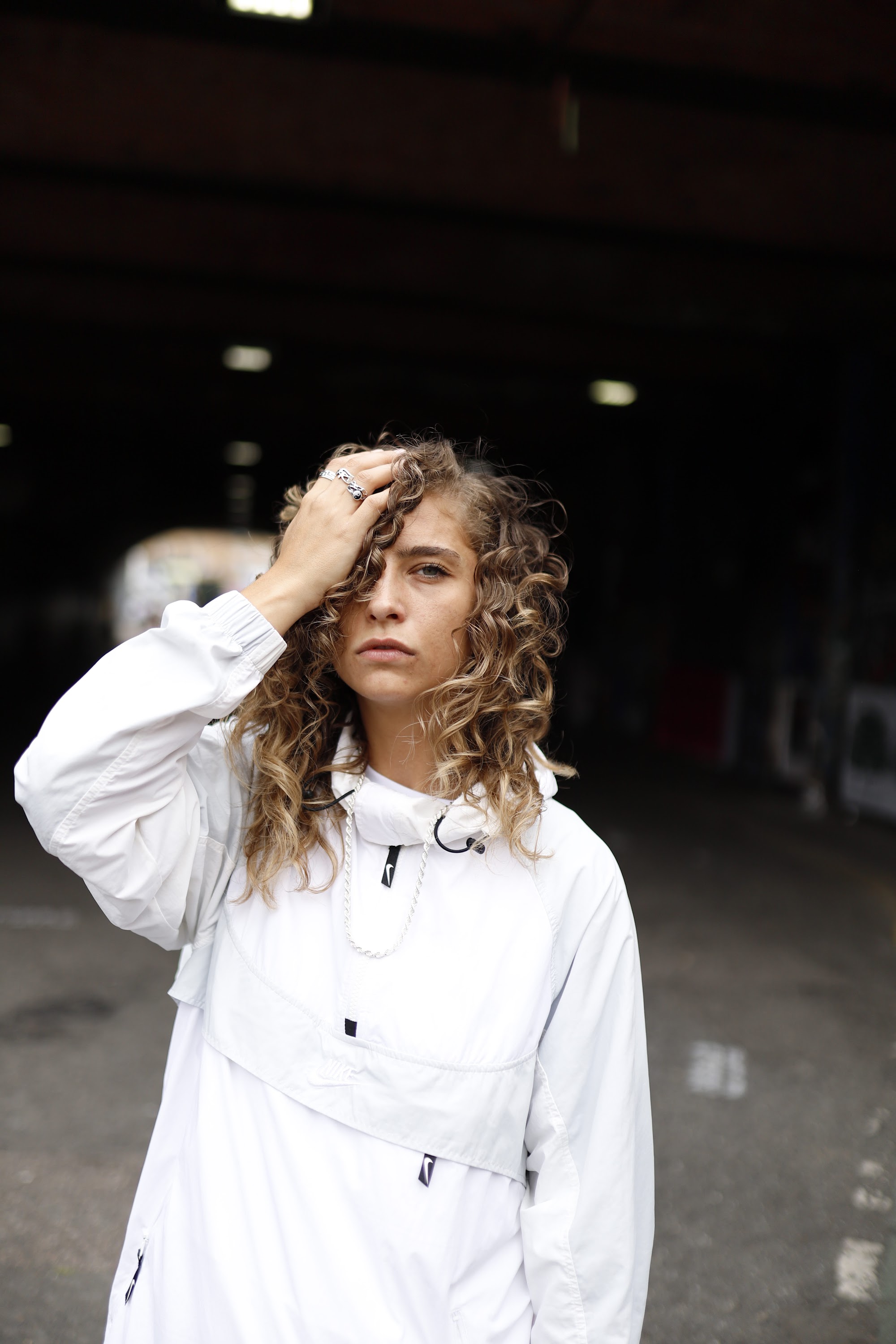 Woman in White Jacket Holding Sunglasses – Dark Urban Tunnel