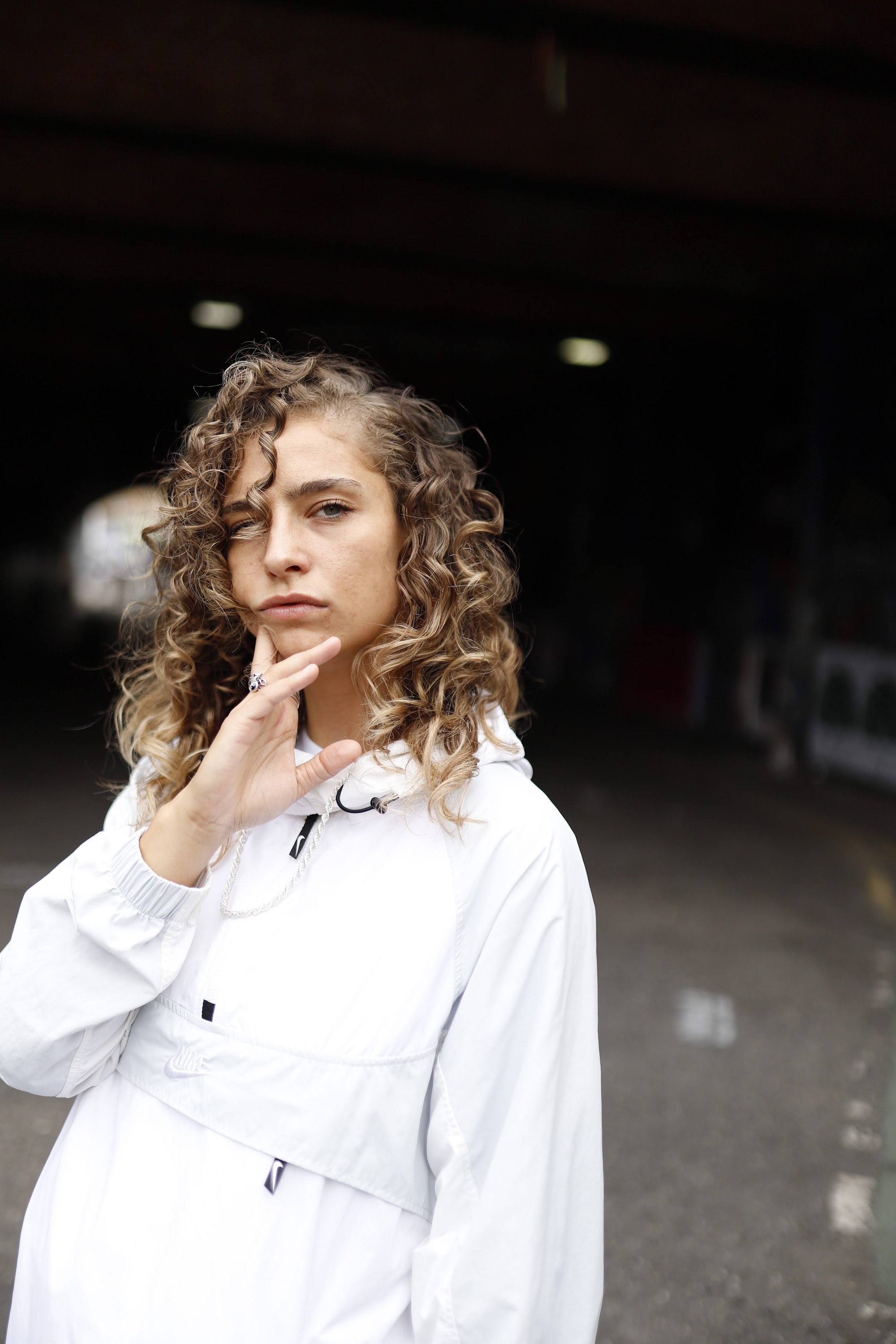 Woman in White Jacket Holding Sunglasses – Dark Urban Tunnel