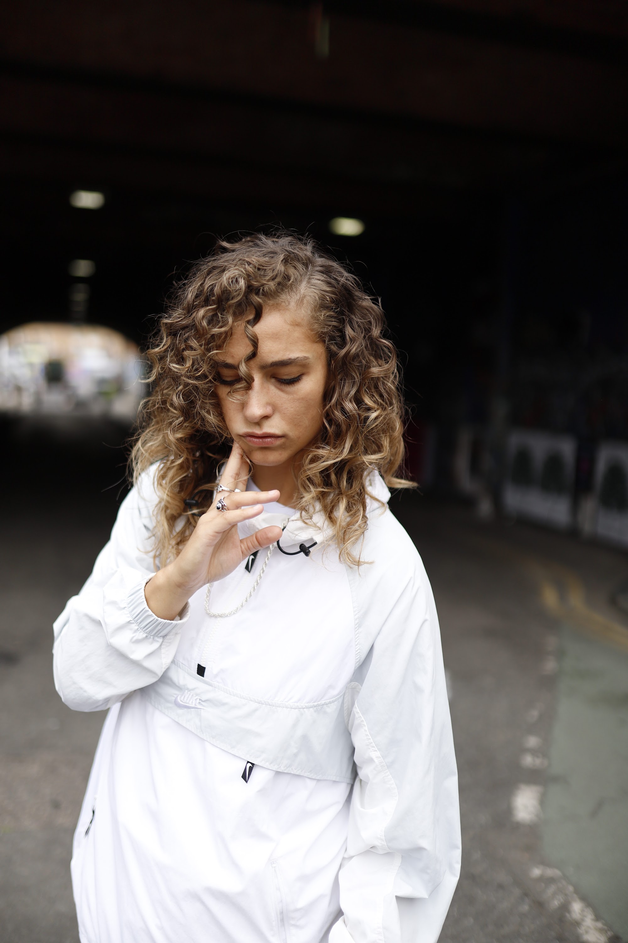 Woman in White Jacket Holding Sunglasses – Dark Urban Tunnel