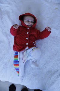 Baby in Red Hooded Jacket Lying on White Quilt