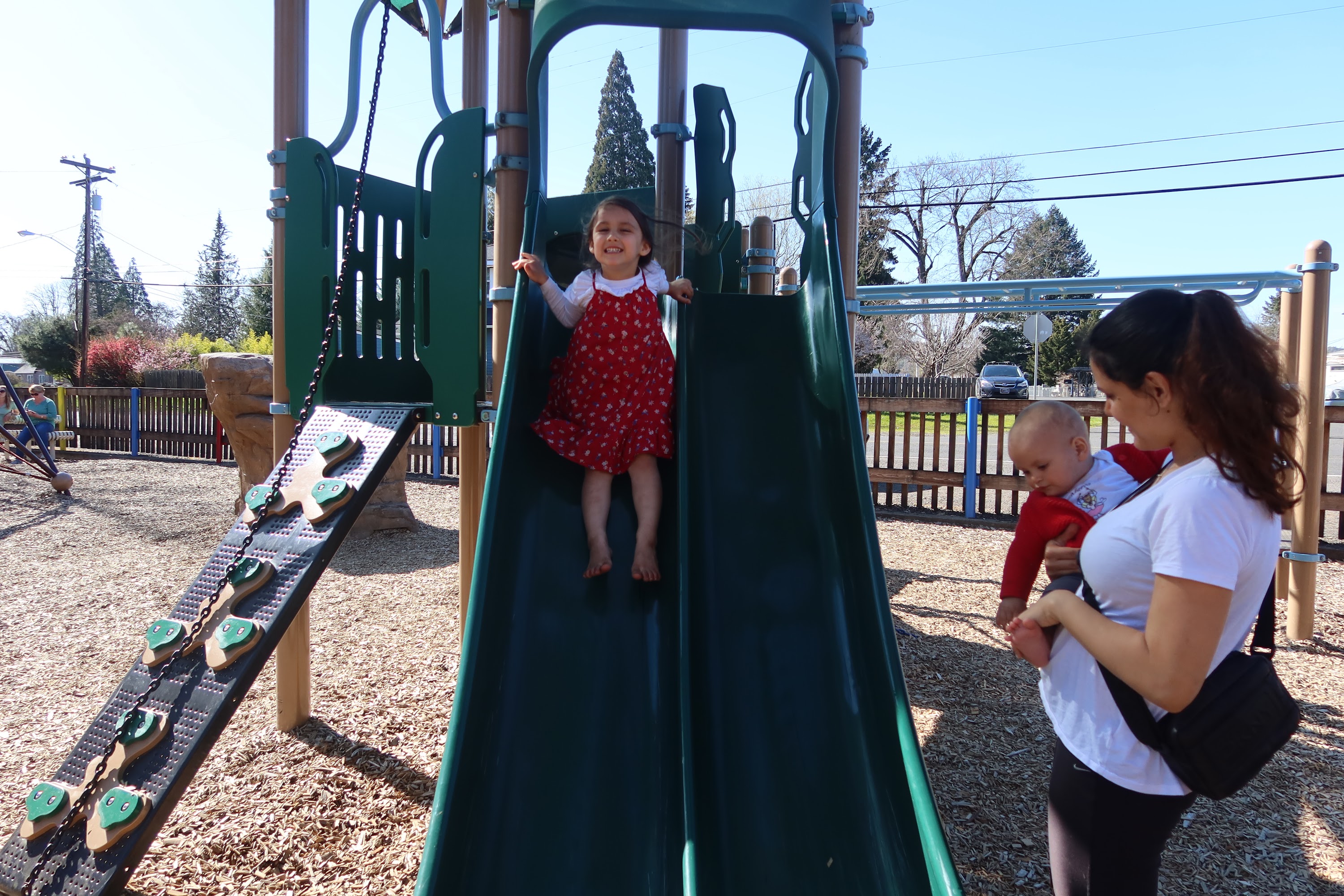 Girl Sliding Down Playground Slide with Mother and Baby